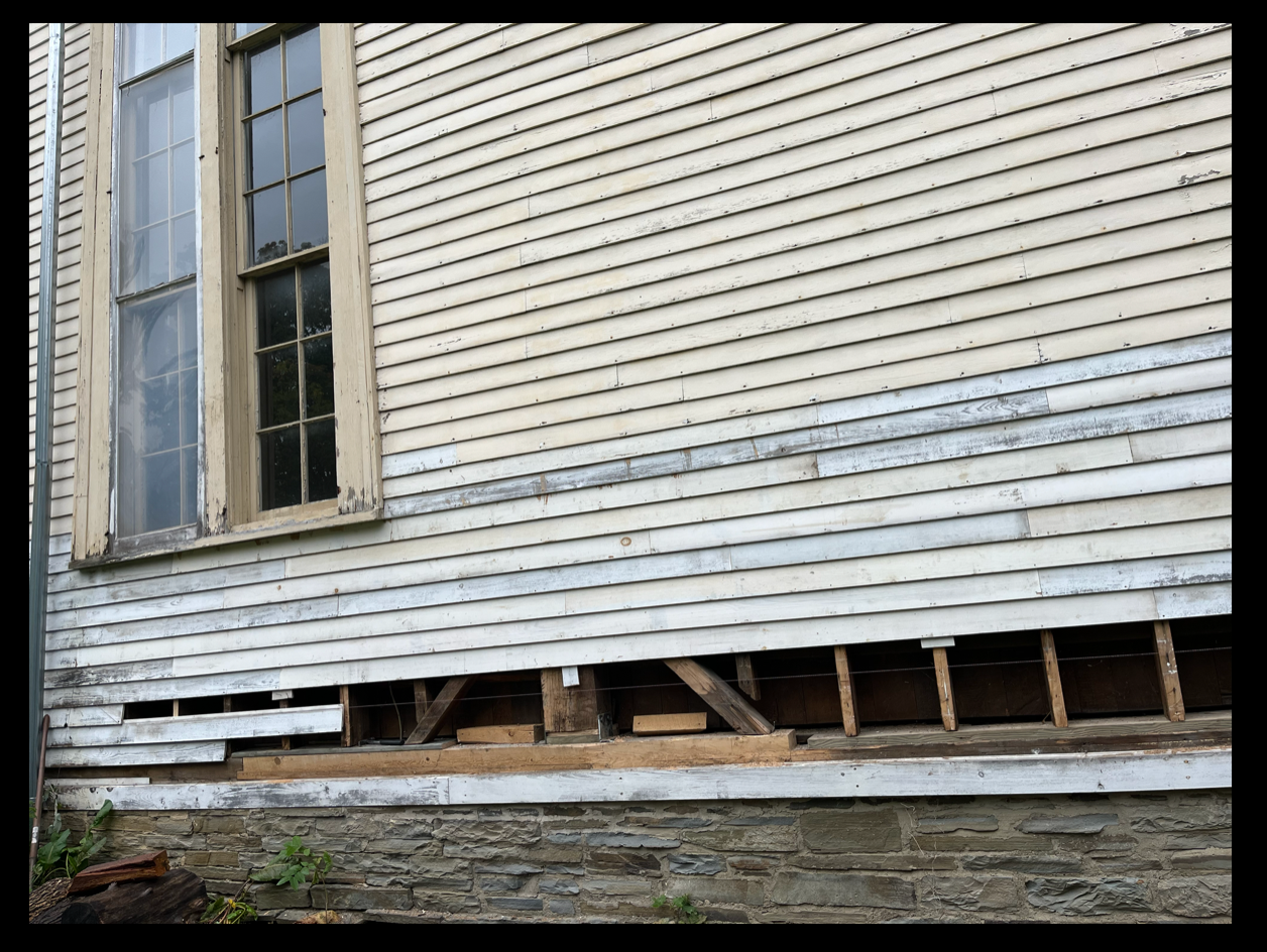 The exterior of the Conservatory with weathered siding, and an unfinished foundation, showing part of the building under renovation.