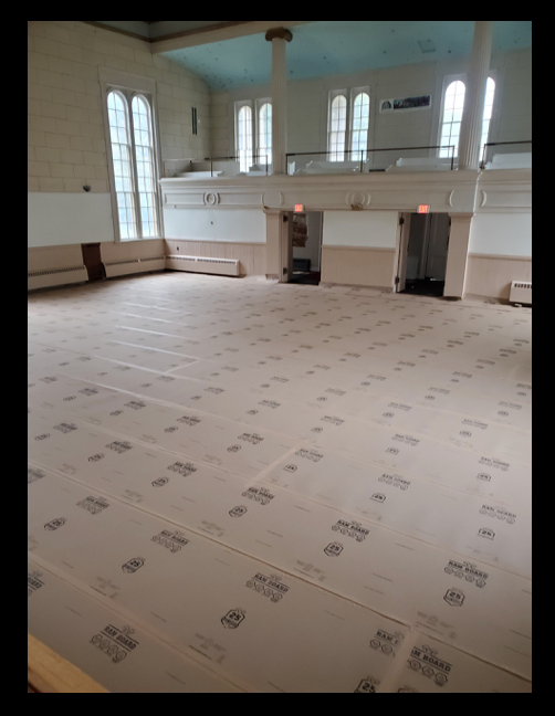 Interior of the Conservatory with large windows, high ceiling, and a balcony area. The floor is covered with protective material and is under renovation or construction.