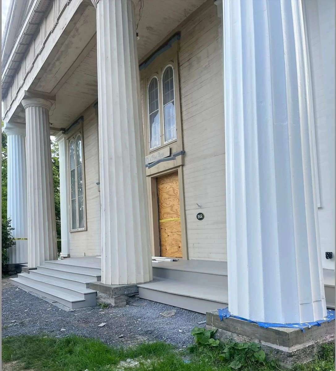 The front of a the TCFA building with tall columns and steps, with a boarded-up doorway and construction tape.