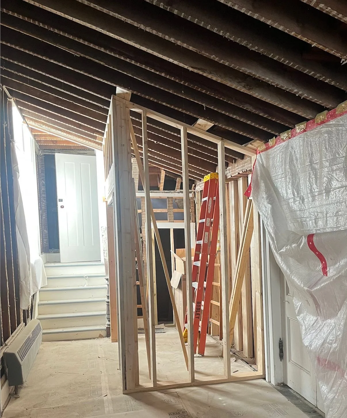 Interior of the foyer under construction, showing wooden framing, a stepladder, and an unfinished ceiling.