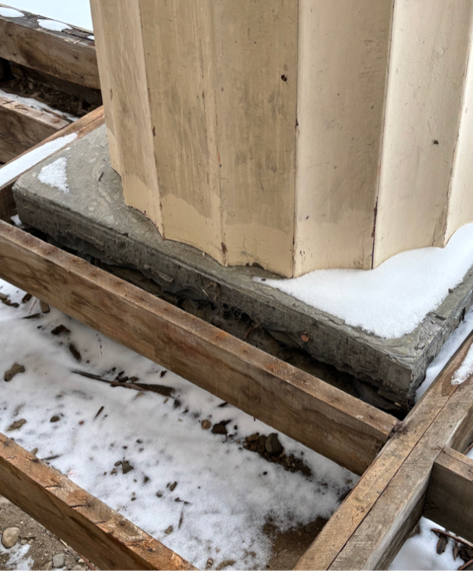 Close-up of a wooden structure with a concrete base, part of a building under construction, with snow on the ground.