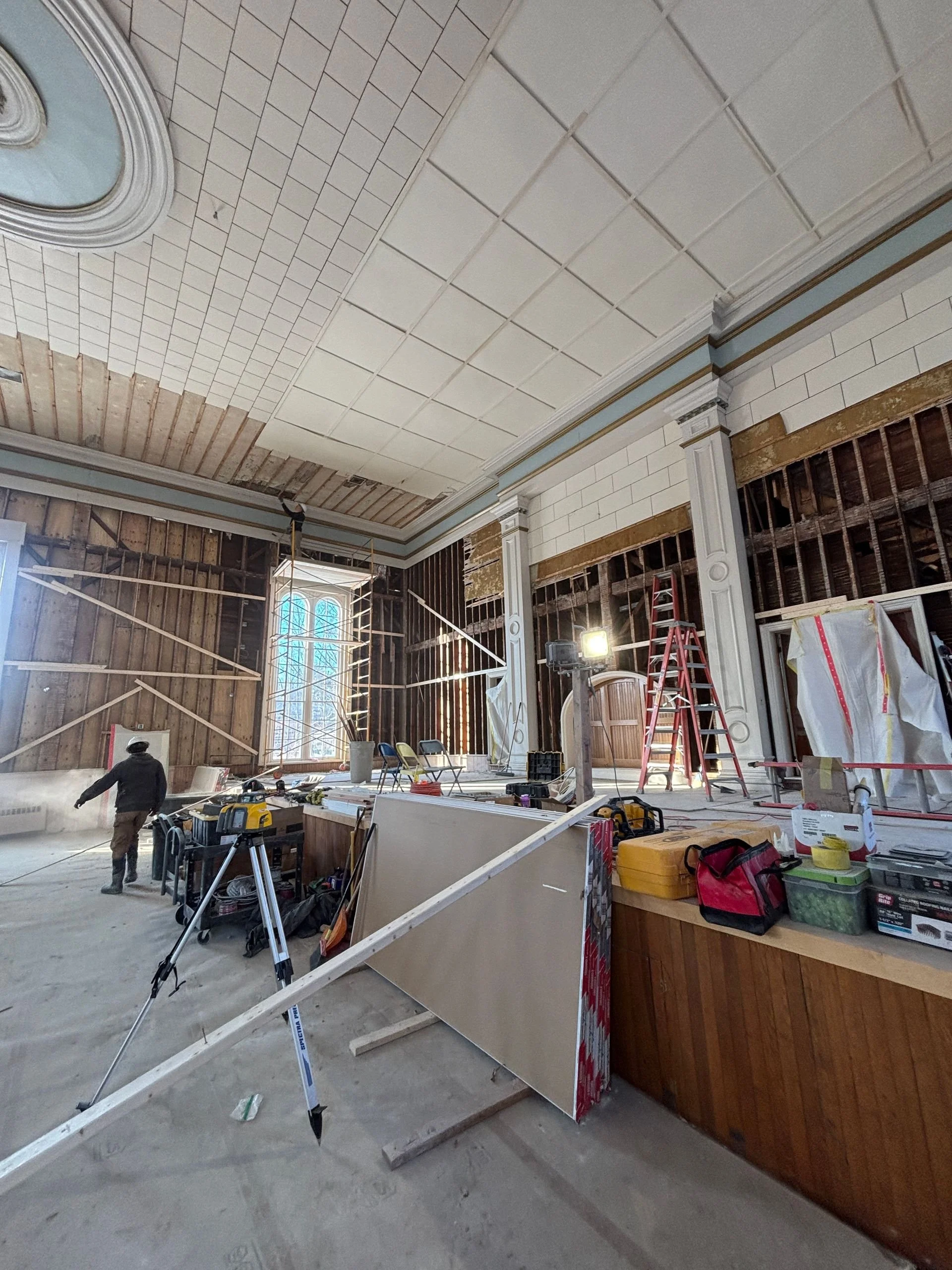 Interior of TCFA under renovation or construction with workers, tools, scaffolding, and unfinished walls and ceiling.