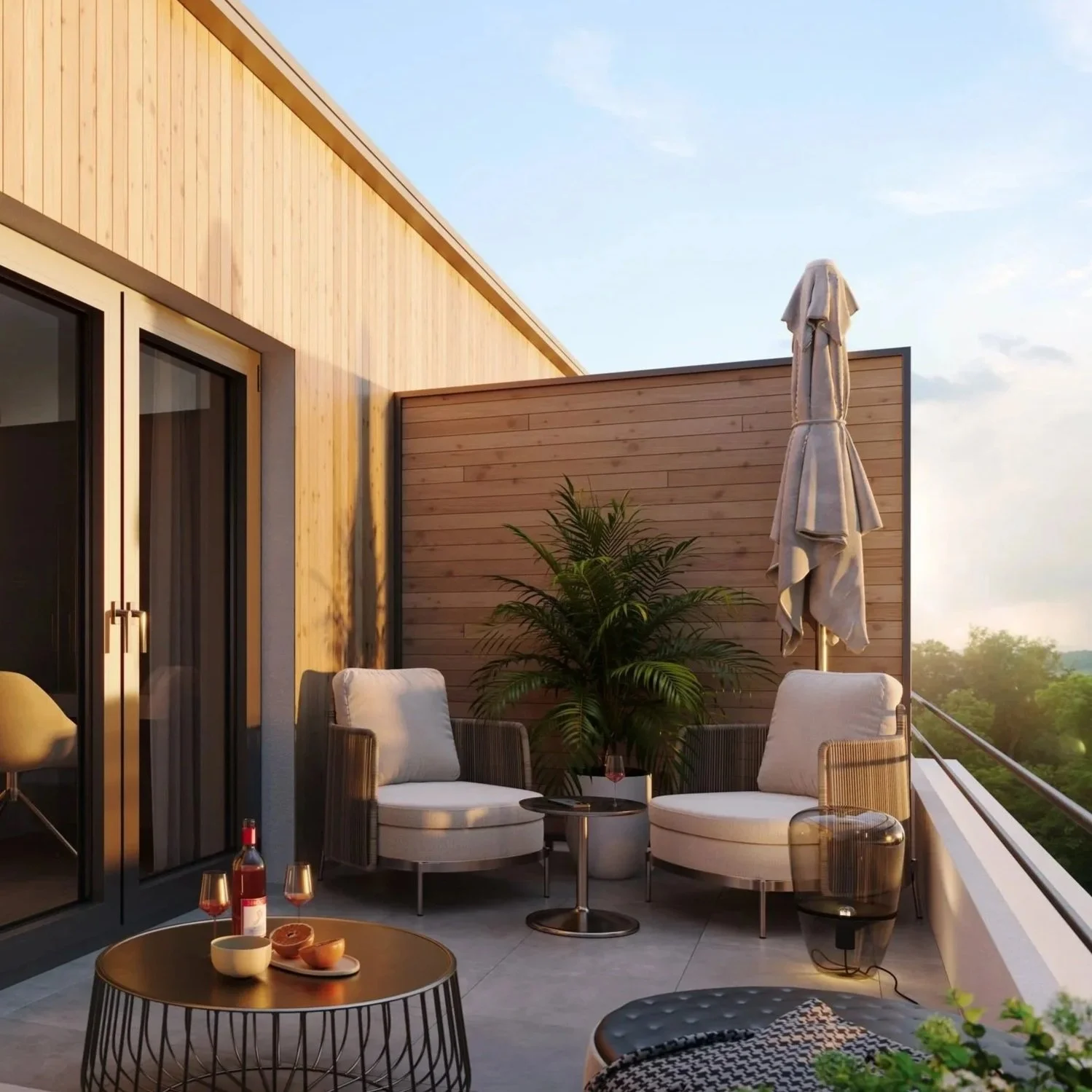 Gemütlicher Balkon mit zwei weißen Sessel, einem kleinen schwarzen Tisch, einer Pflanzen und einem großen geschlossenen Sonnenschirm bei Sonnenuntergang, Blick auf Bäume im Hintergrund.