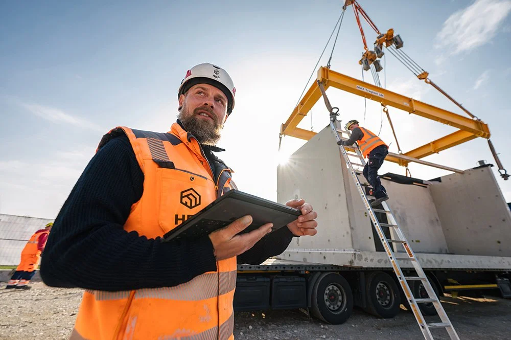Bauarbeiter mit Tablet überwacht Baumaschine, während in der Baustelle anbetracht wird