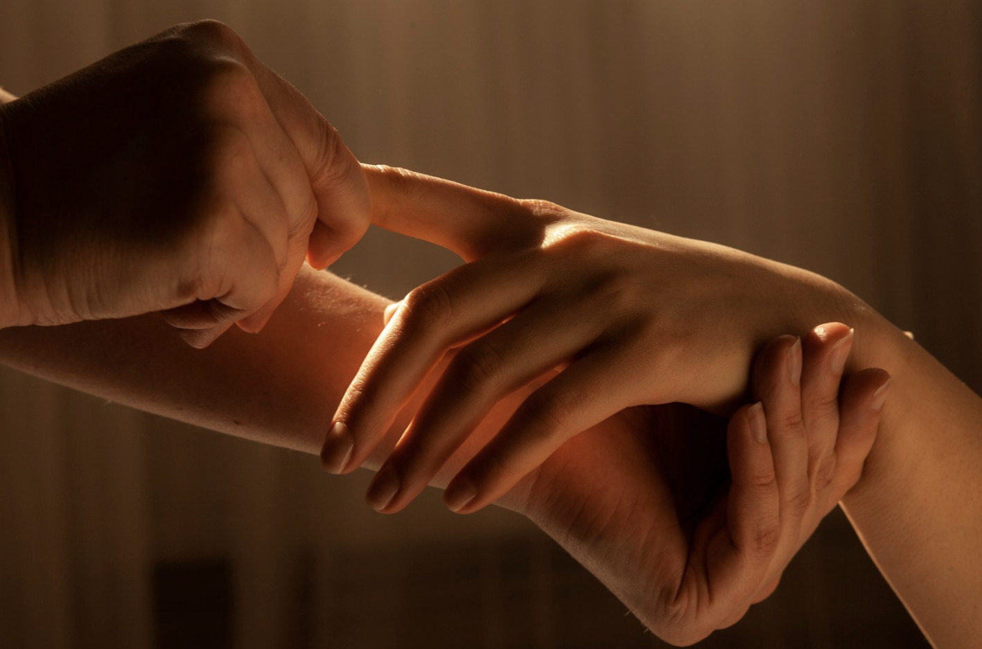 Two hands gently holding each other, with one hand touching the other's wrist, illuminated by warm, soft lighting.