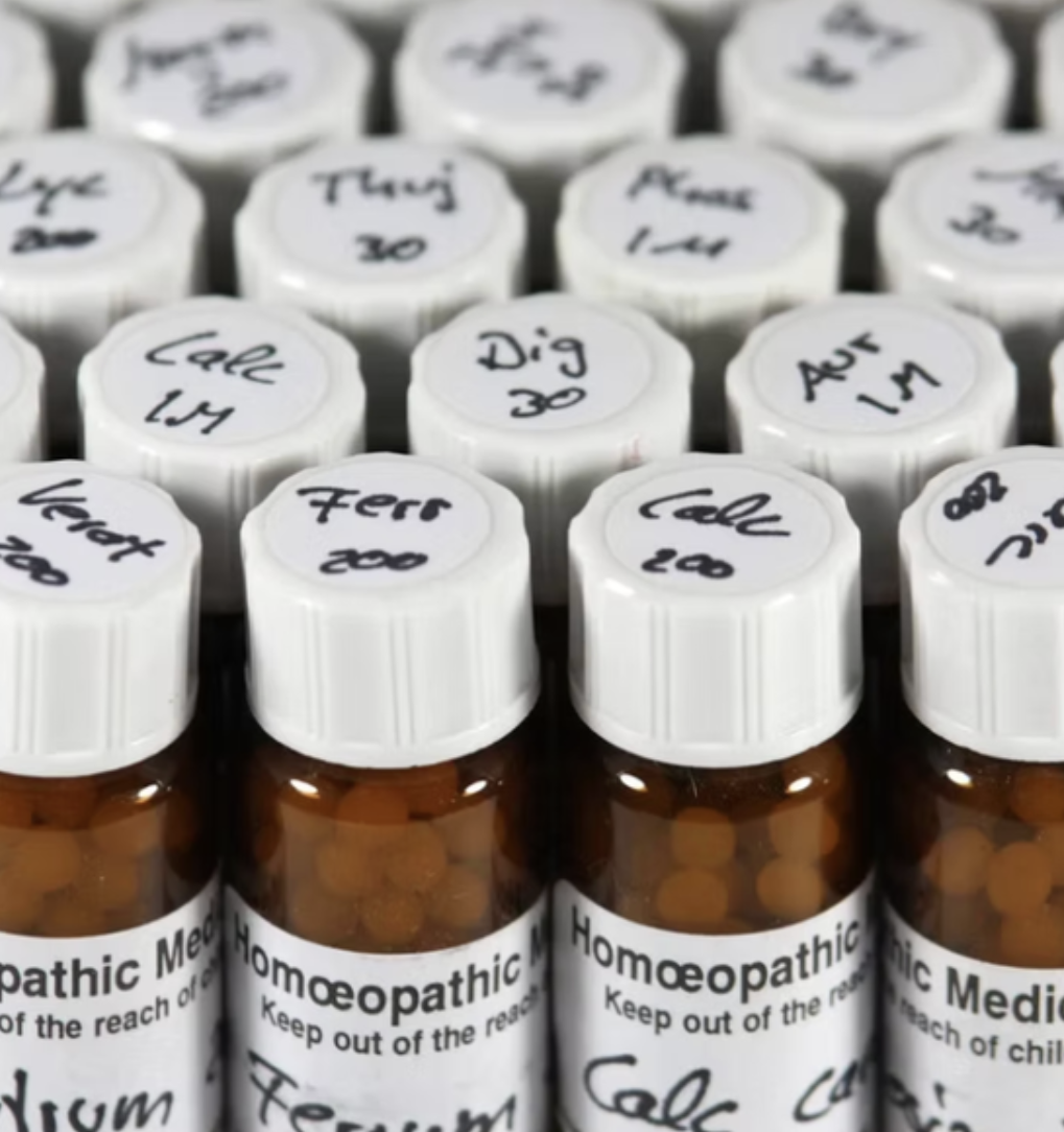 Collection of brown homeopathic remedy bottles with white caps and handwritten labels indicating different remedies.