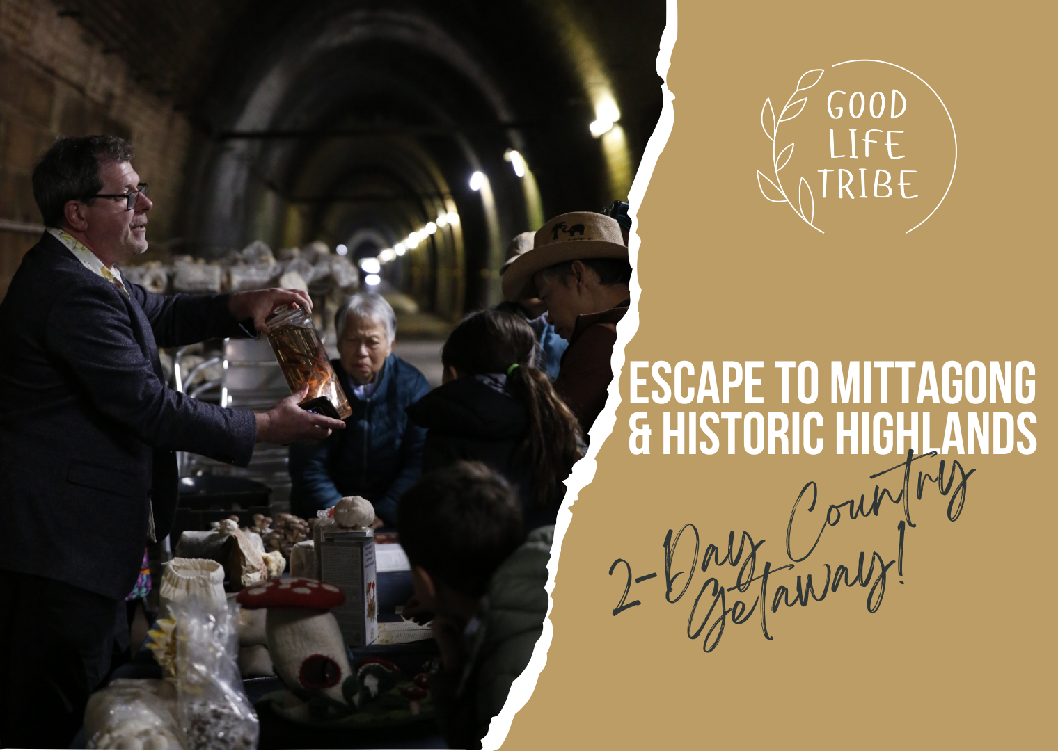 A man with glasses and a dark jacket holds a jar of mushrooms, speaking to a group of people inside a tunnel. The group includes a woman with a hat and a child, and they are gathered around a table with various mushroom products for sale.