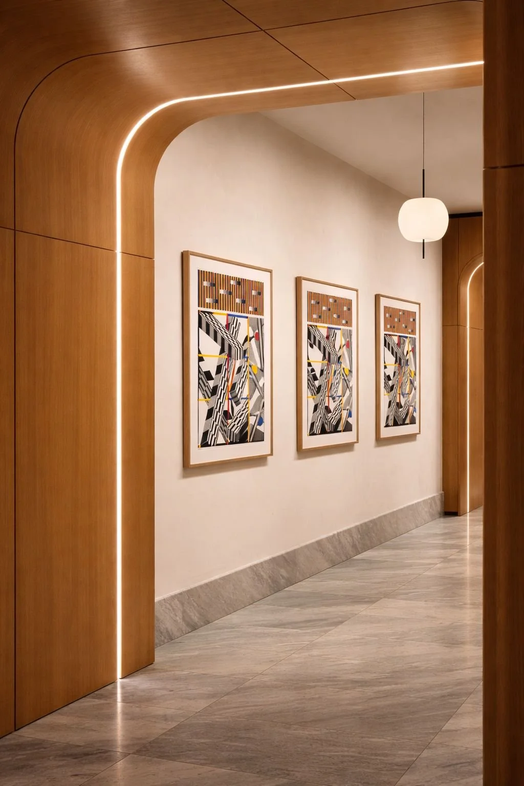 A hallway with wooden archways, three abstract art pieces hanging on a white wall, a hanging light fixture, and a tiled floor.