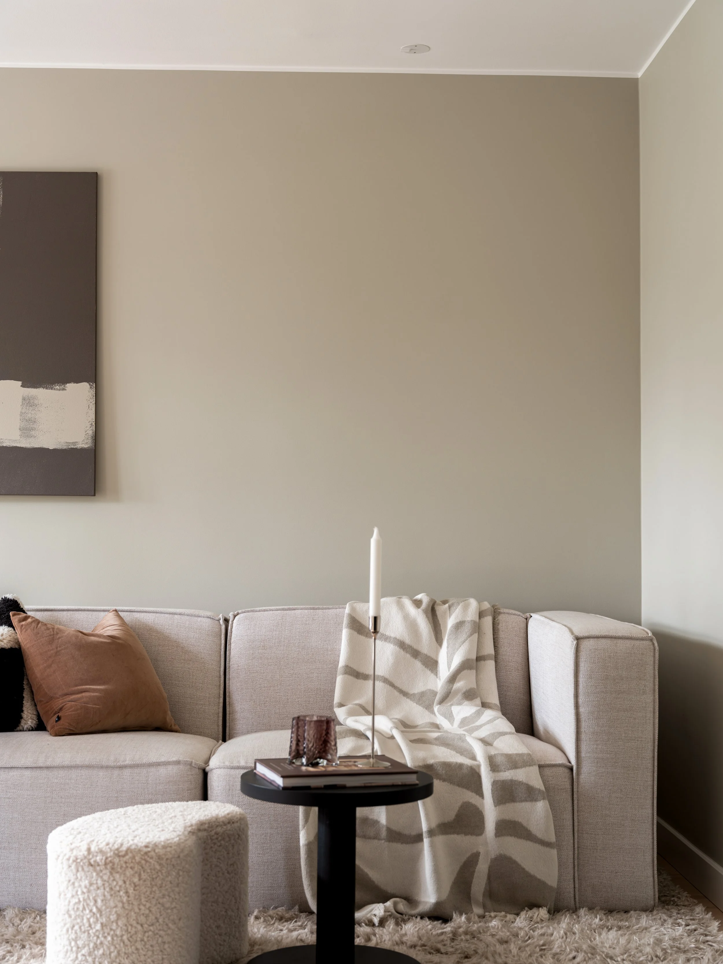 Stue med beige sofa, skulptur, lysestake, bok, pute og teppe.