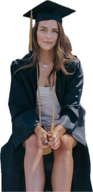 Young woman wearing a graduation cap and gown, sitting with her knees up, holding her tassels, smiling.