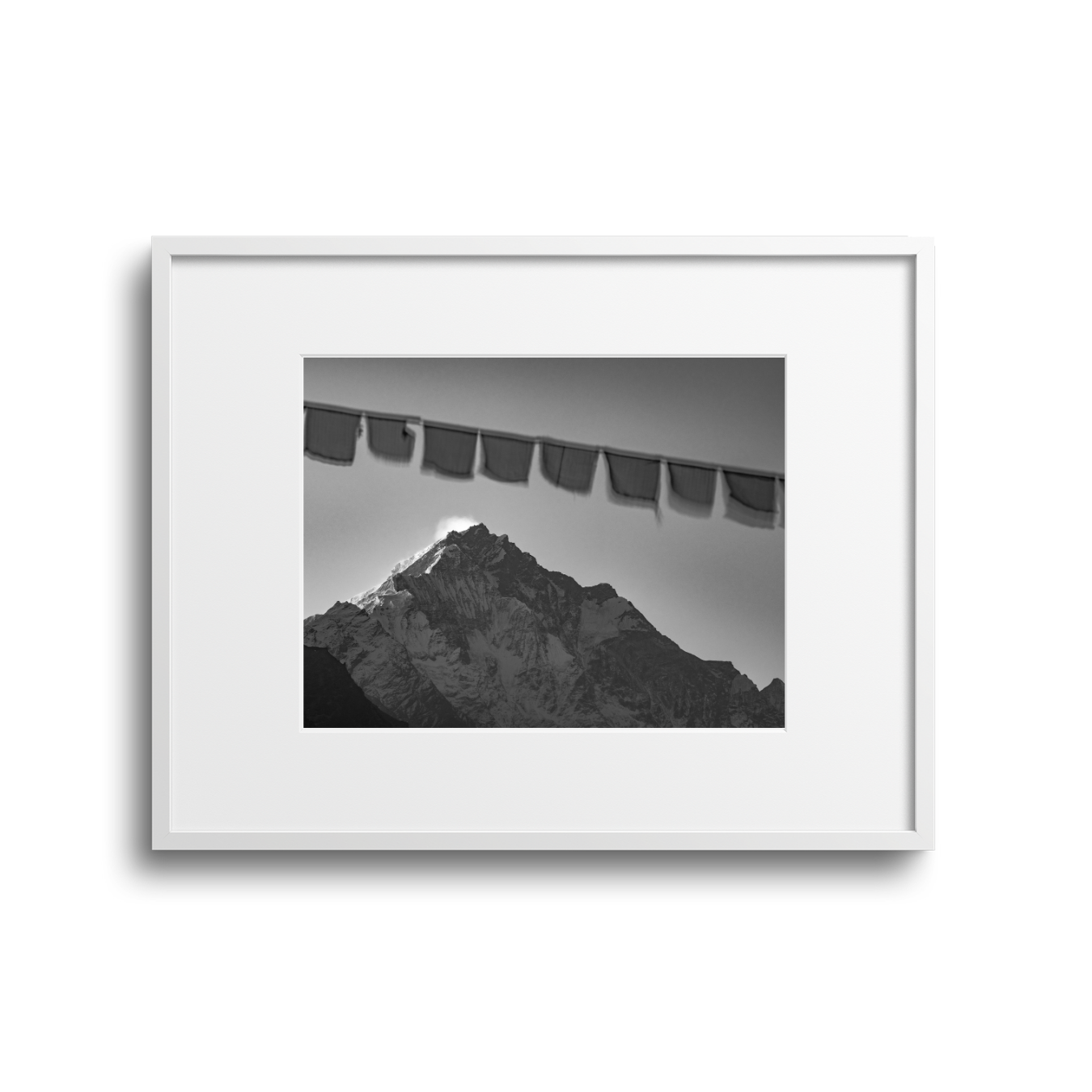 Black and white framed photograph of a mountain with snow, with prayer flags hanging above.