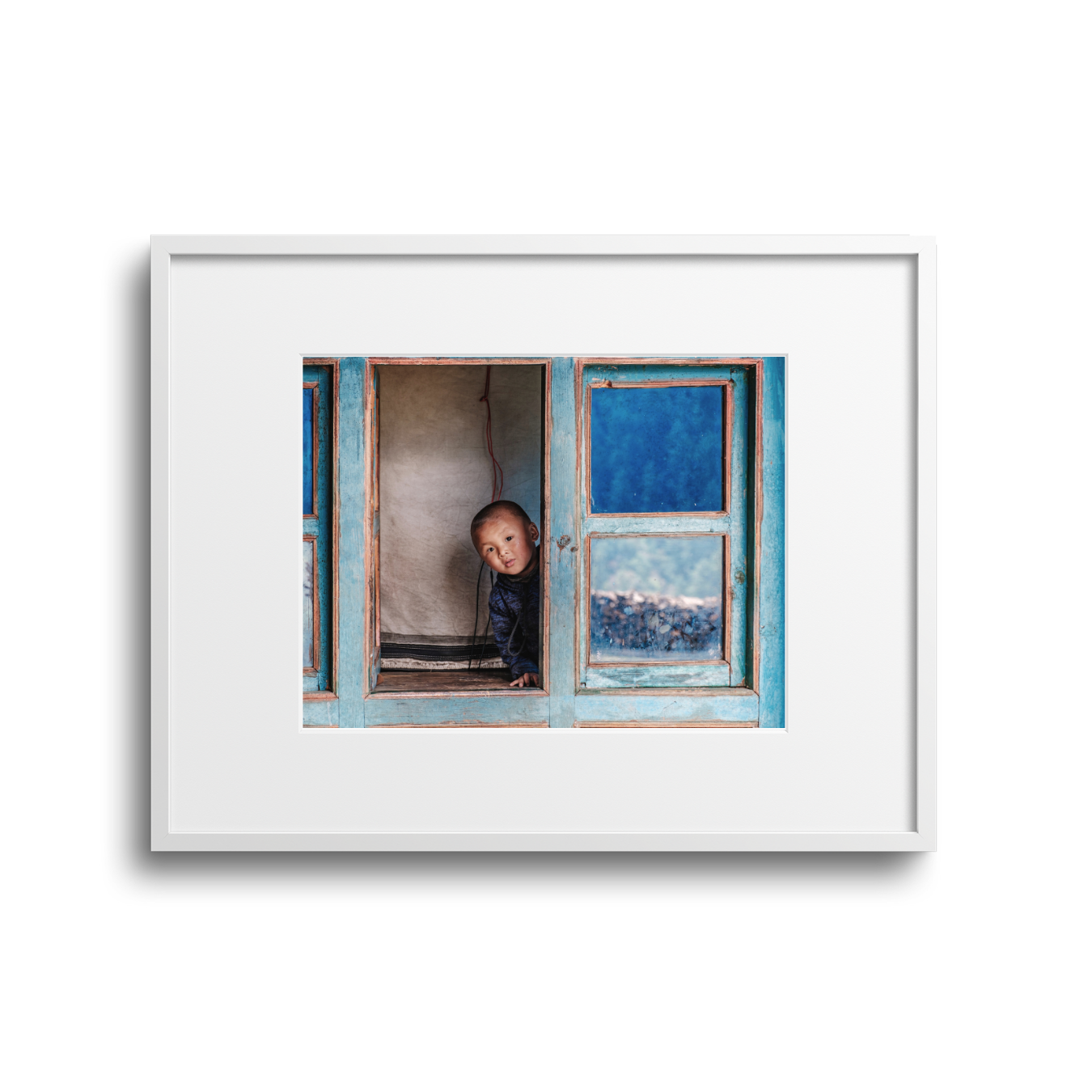 A young child peeking out of a slightly open window with blue wooden framing and glass panes, in a rustic setting.