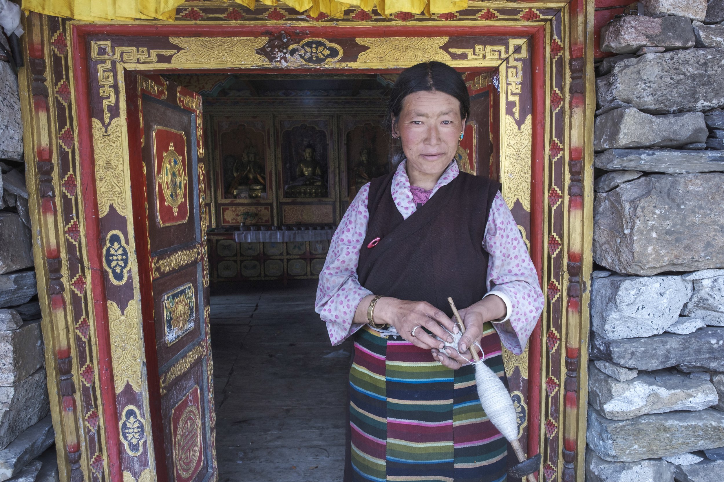 Woman standing in the doorway of a monastery holding a spindle in Tsum Valley, Nepal.