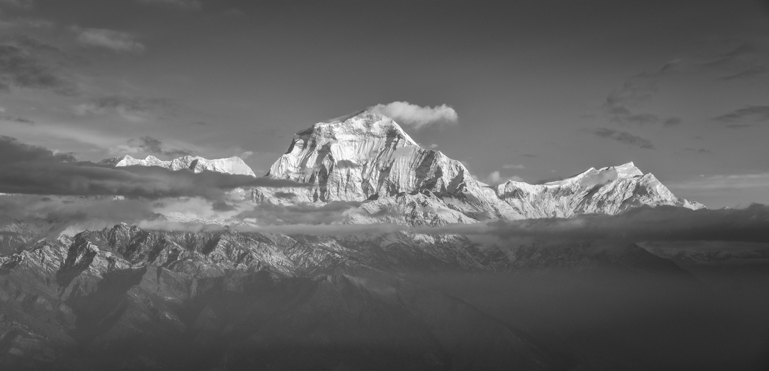 Black and white photo of a snow-capped mountain range with clouds around the peaks.