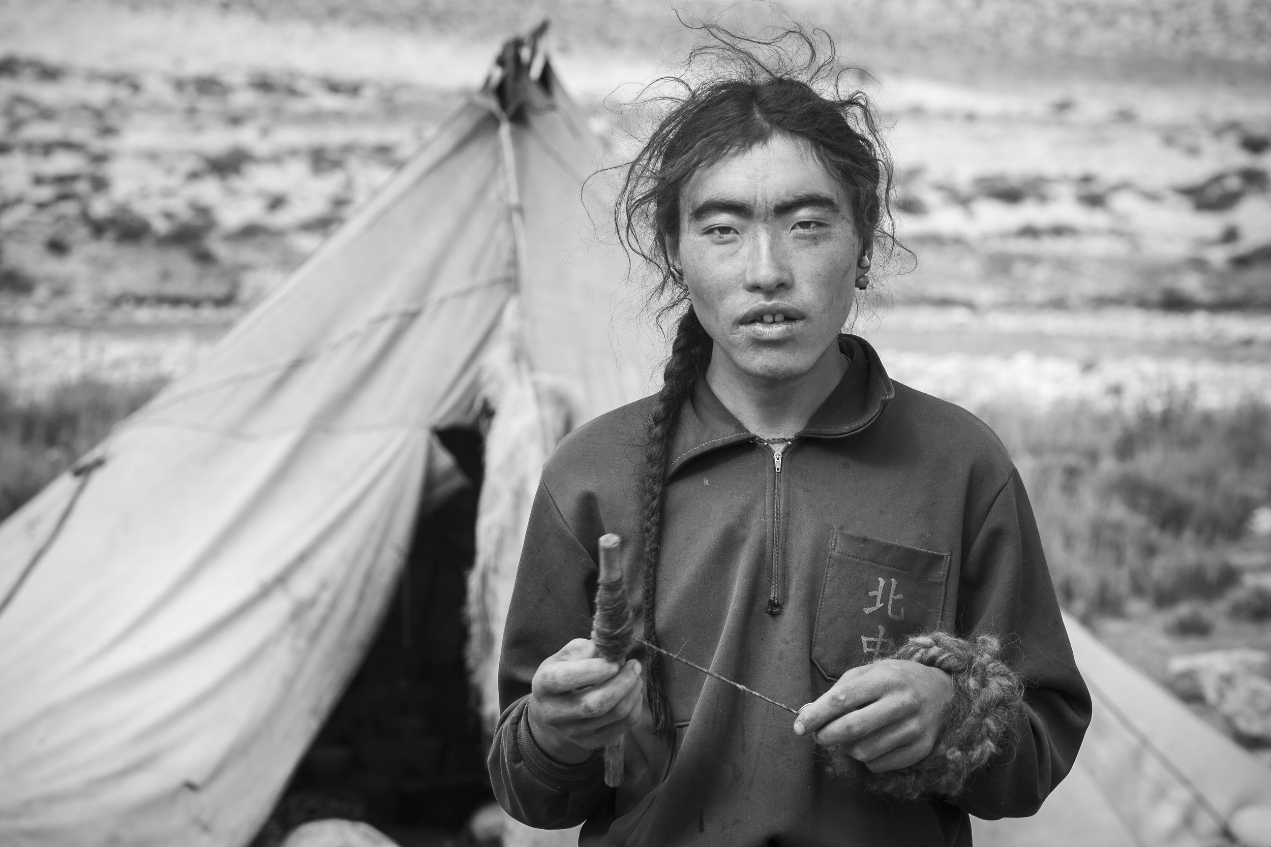 Young nomad man spinning wool thread by hand outside a tent on the Tibetan Plateau.