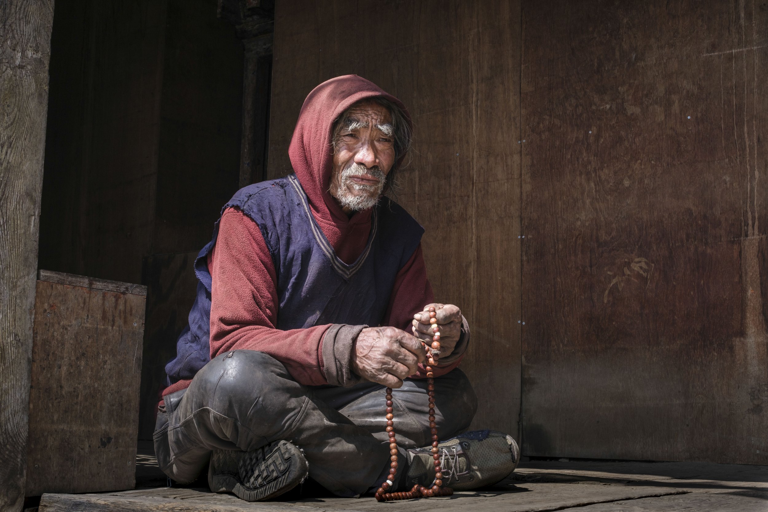 Old Sonam sits at the doorway of Mu Gompa, prayer beads resting in his weathered hands. Though often lost in drink, he remains a helpful presence at the monastery — gathering firewood, tending small chores, and lingering between devotion and solitude