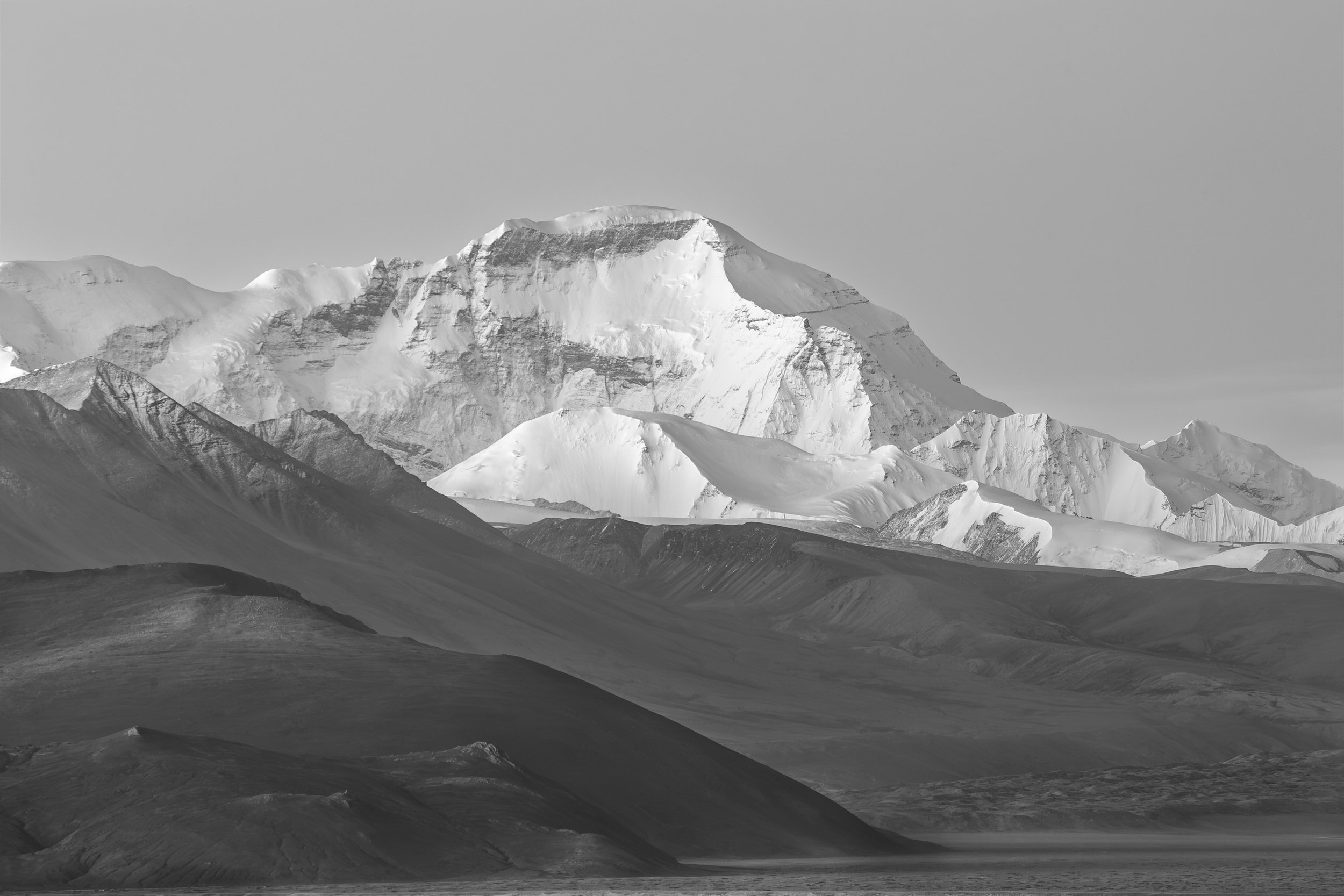 Snow-covered Himalayan peak rising above layered ridges on the Tibetan Plateau.