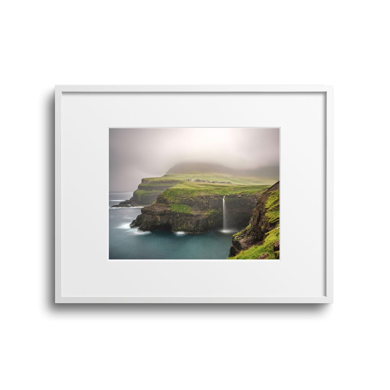 Landscape photograph of a rugged coastline with green cliffs, waterfall, and misty weather.