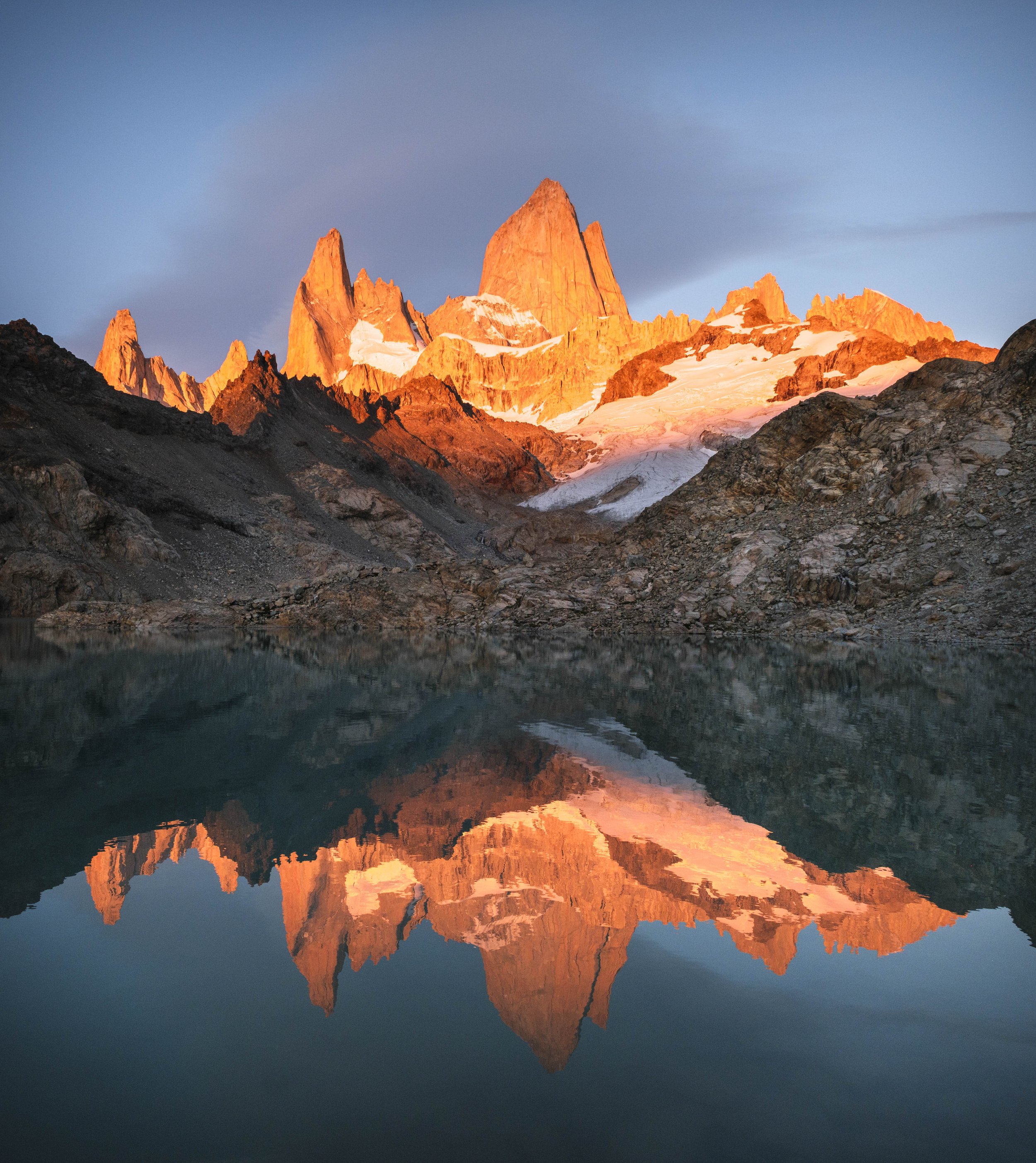 Sunrise light illuminating jagged alpine peaks reflected in a still mountain lake in Patagonia.