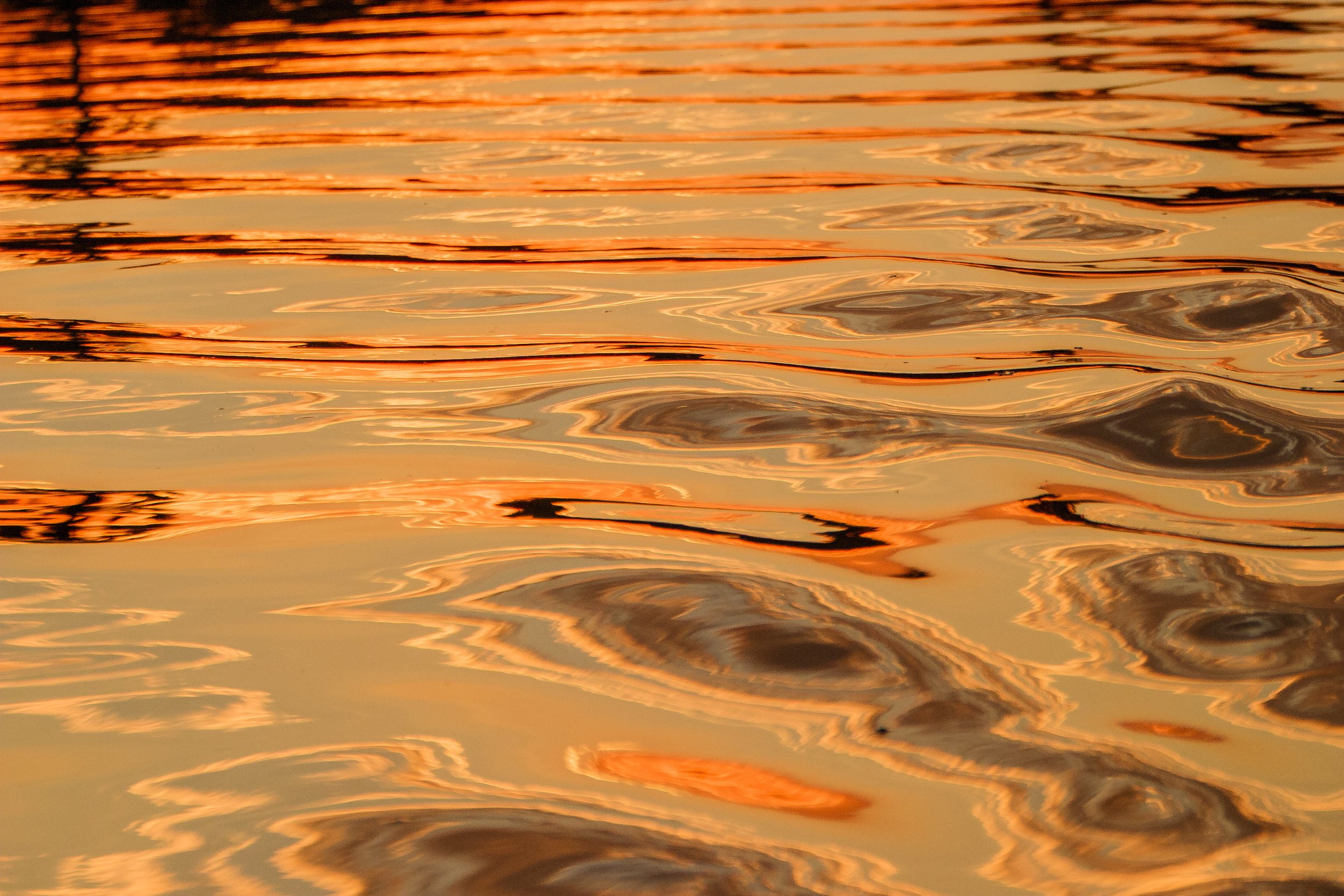 Abstract patterns of orange light reflecting on rippling water surface.
