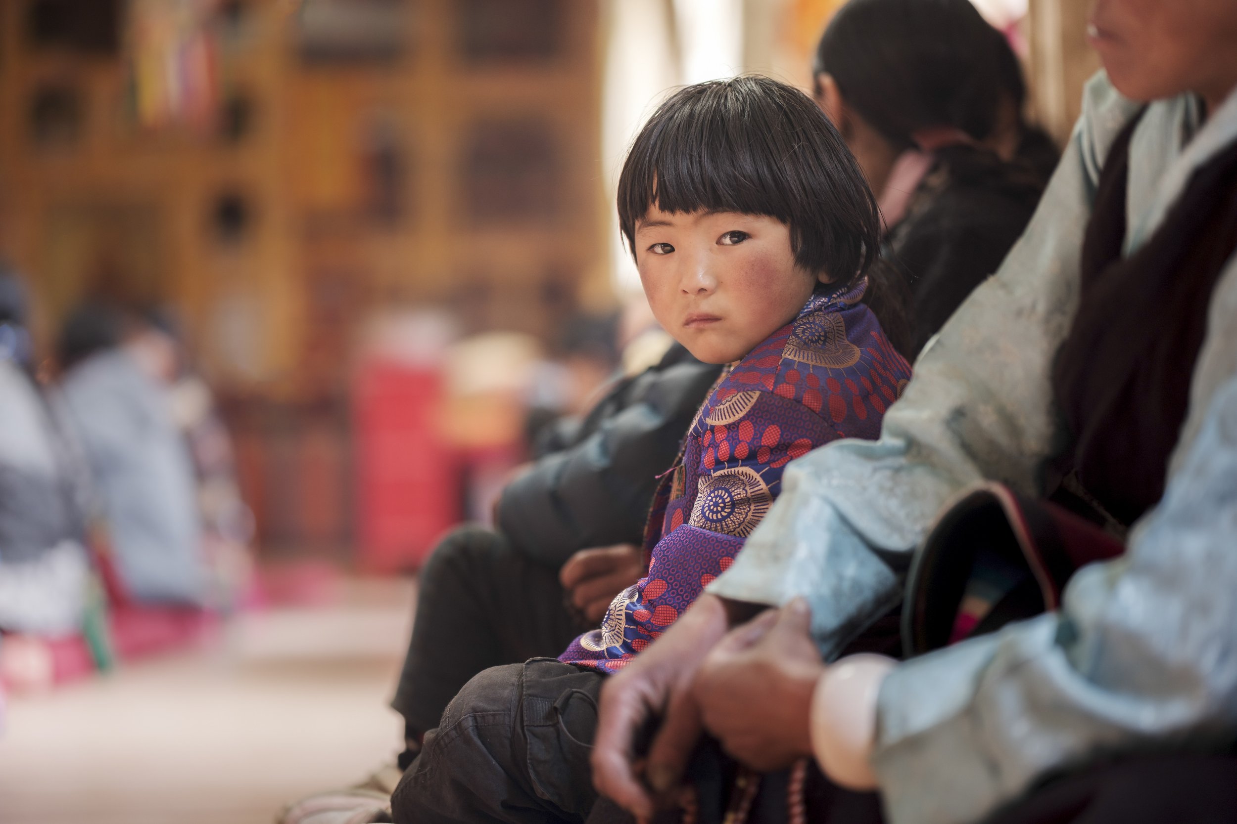 Young child seated among adults inside a monastery during a communal gathering in Tsum Valley, Nepal.