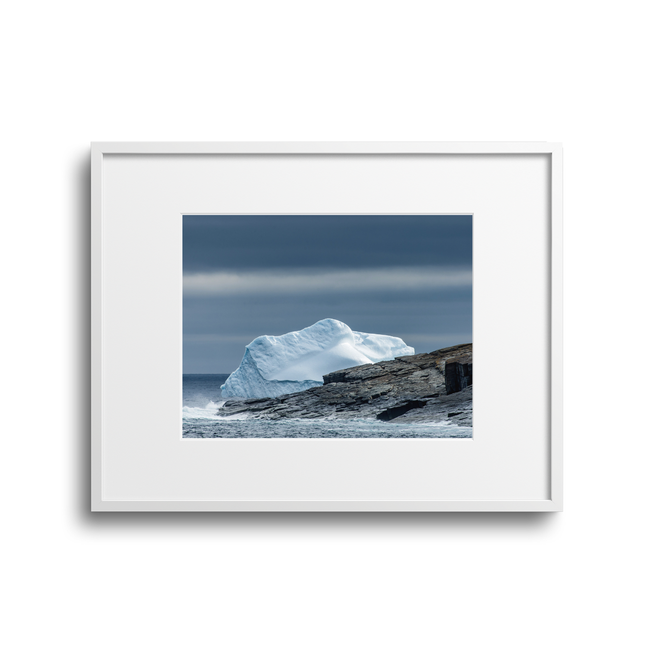 Photograph of an iceberg resting on rocky shoreline under a cloudy sky.