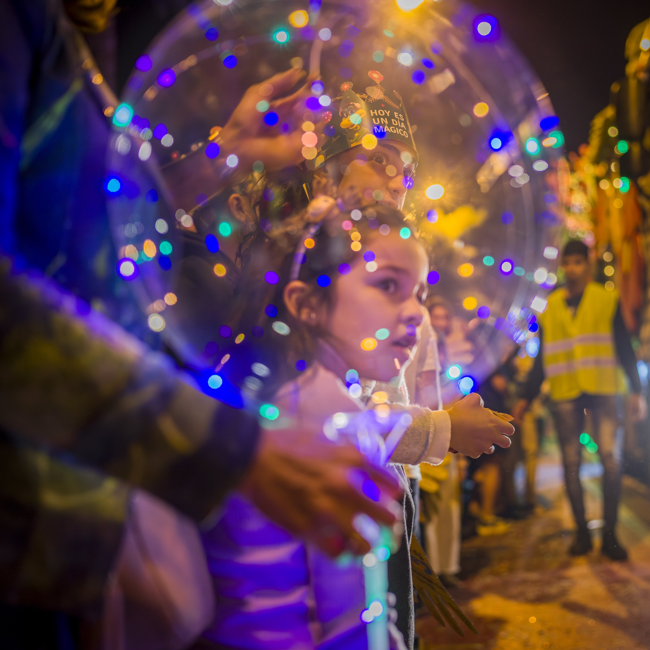 Child seen through a transparent balloon with colorful lights at night during a public celebration.
