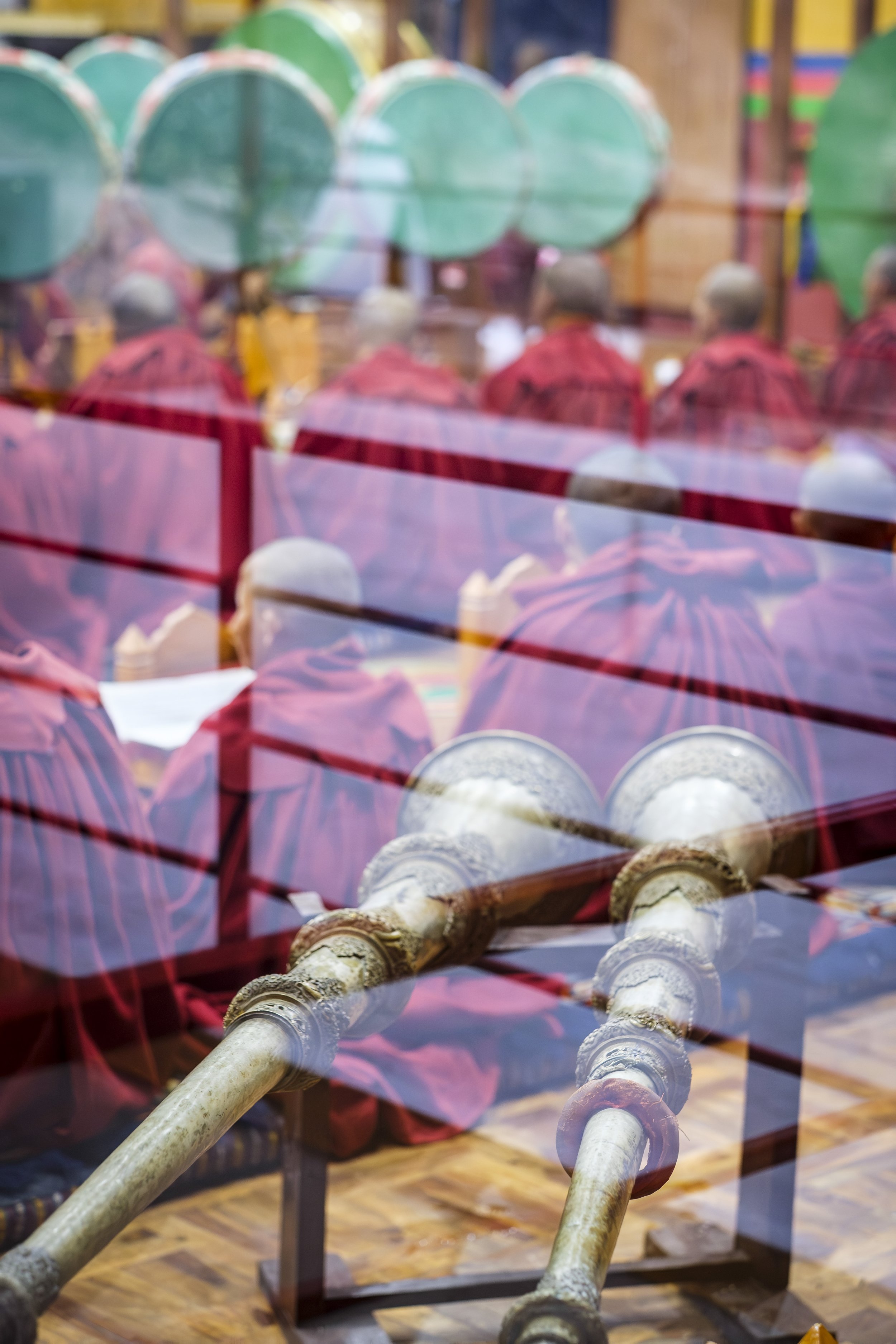 Tibetan monks seen through reflective glass with ceremonial horns in the foreground.