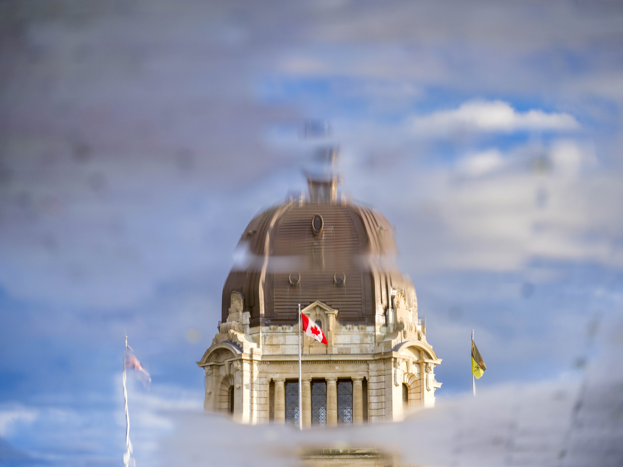 Domed building with a Canadian flag viewed through rippling water creating visual distortion.