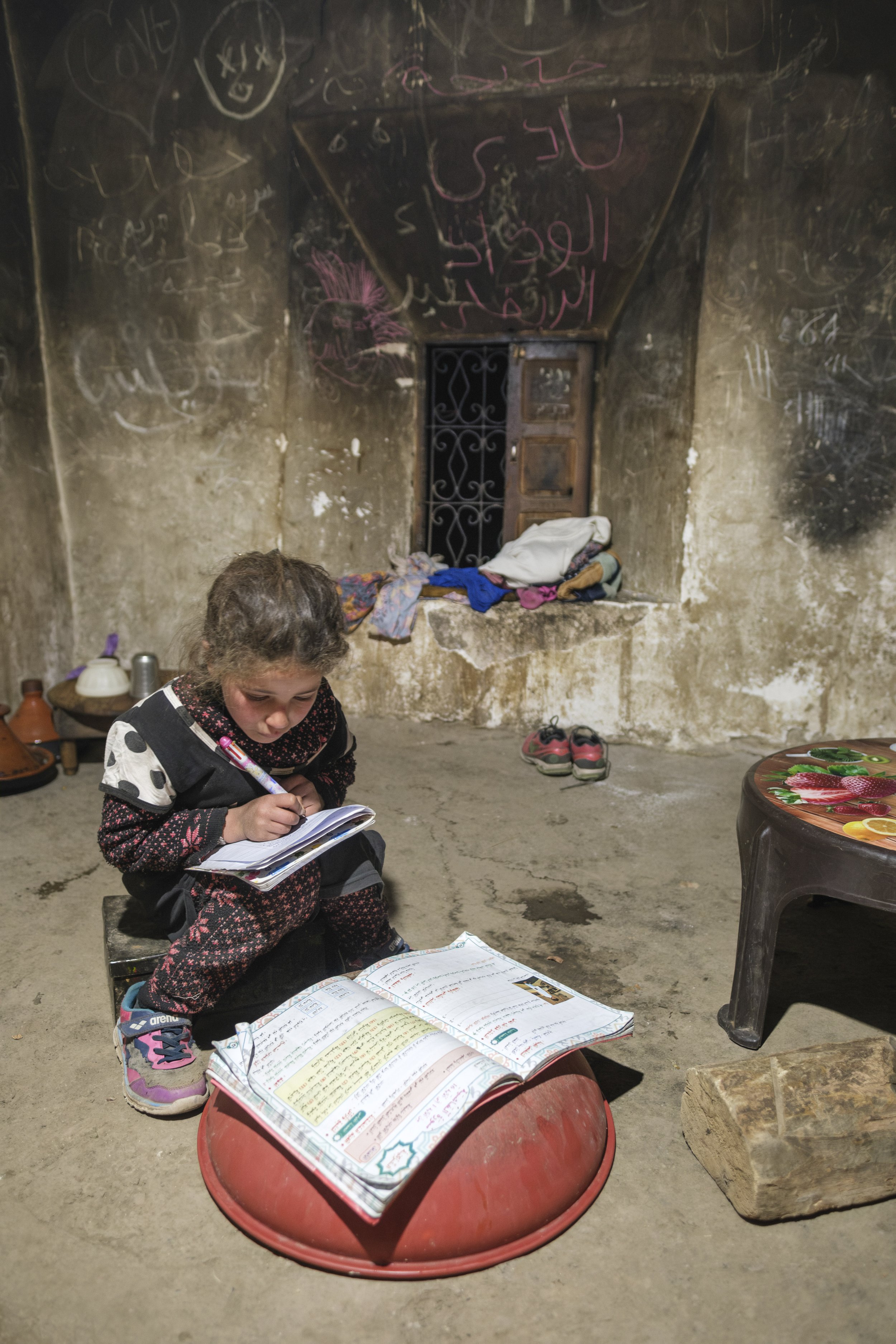 Young girl studying and writing in a notebook inside a rural home in the Aït Bouguemez Valley in Morocco’s High Atlas Mountains.
