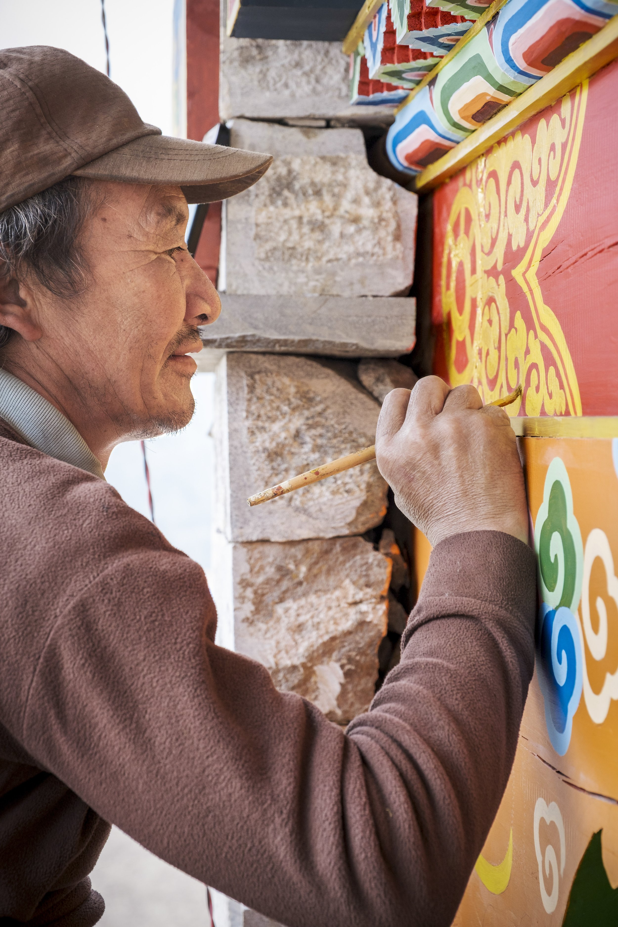 Artisan painting traditional decorative patterns on a monastery wall in Tsum Valley, Nepal.