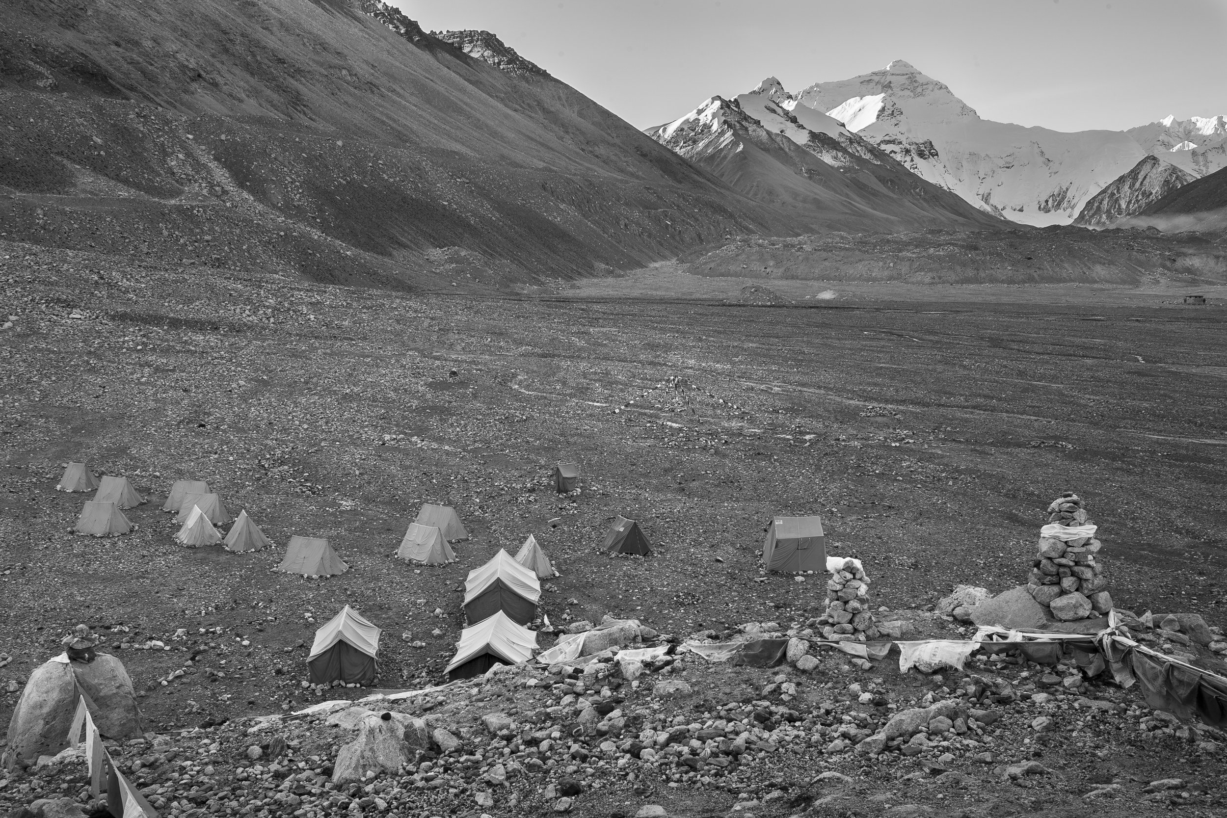 High-altitude campsite with tents and stone cairns in a barren Himalayan landscape.