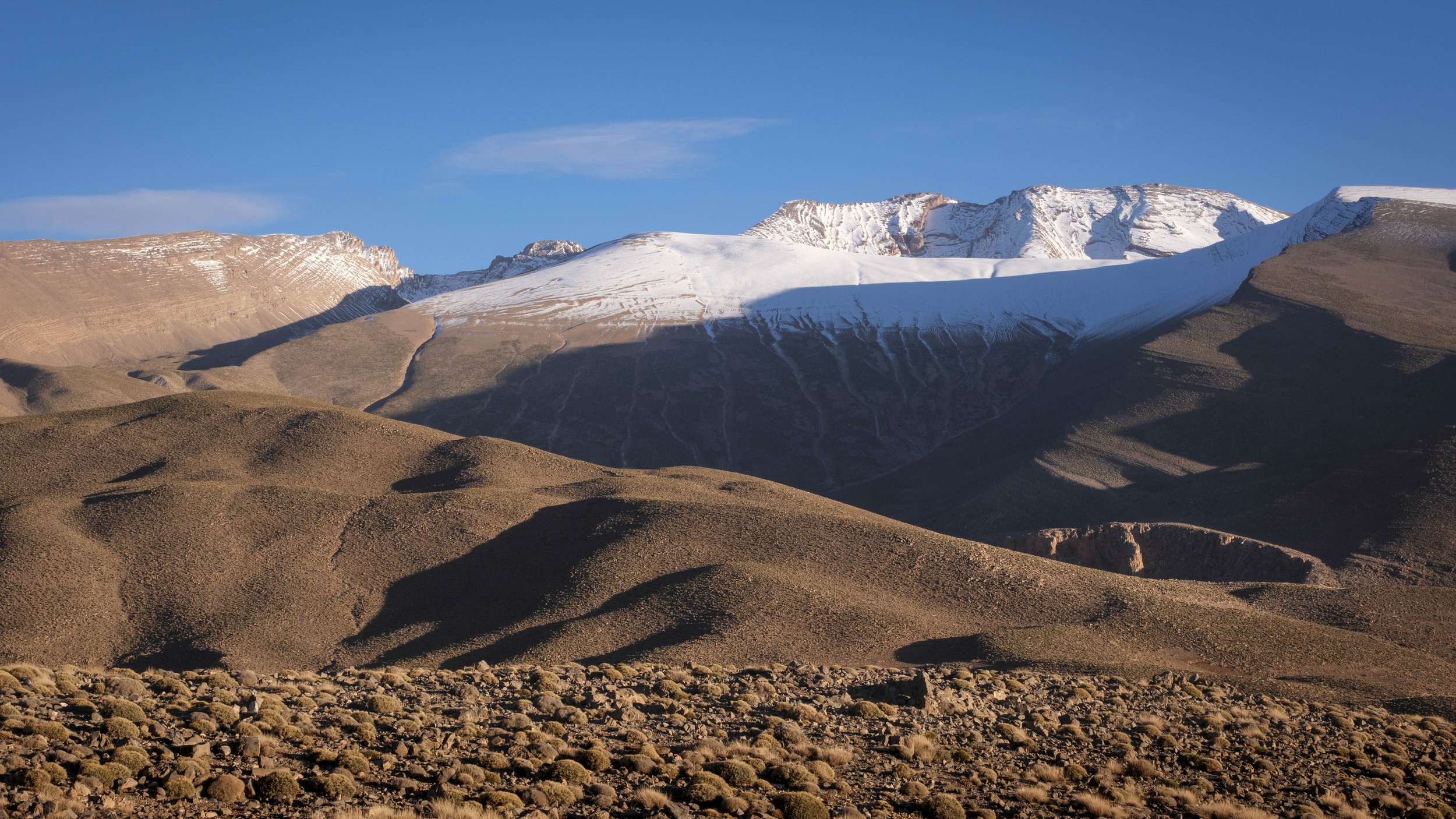 Snow-covered peaks rising above arid mountain slopes in the High Atlas Mountains of Morocco.