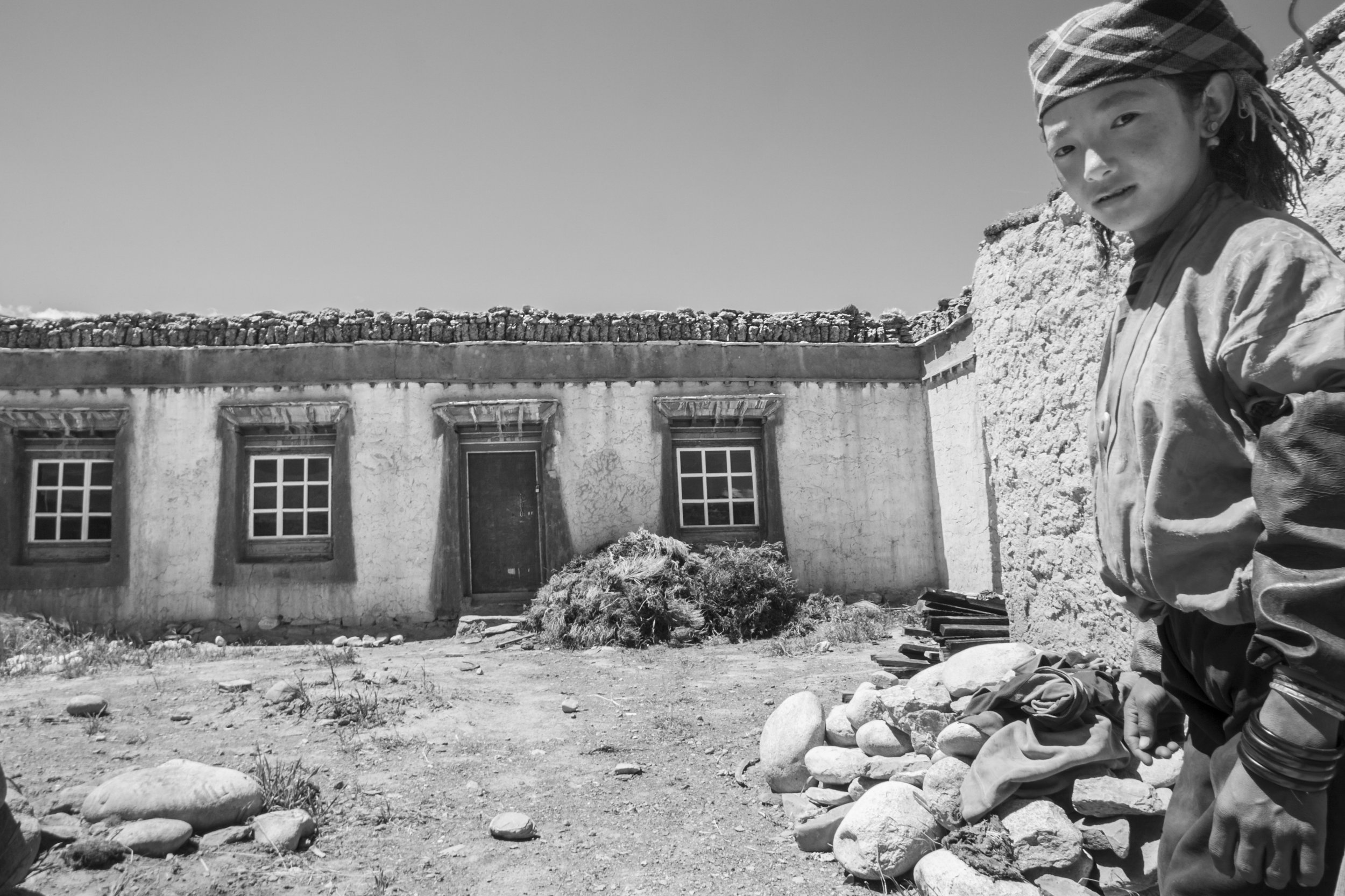 Young girl standing beside a stone house in a rural village on the Tibetan Plateau.