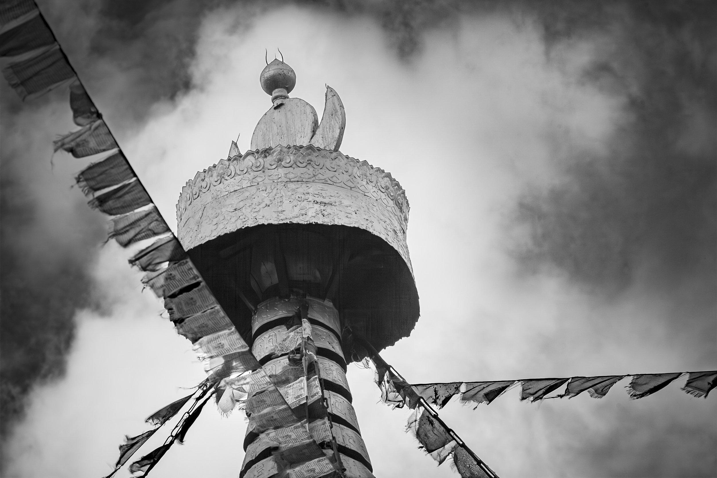 Buddhist stupa with flags against a cloudy sky in the Tibetan Himalayas.