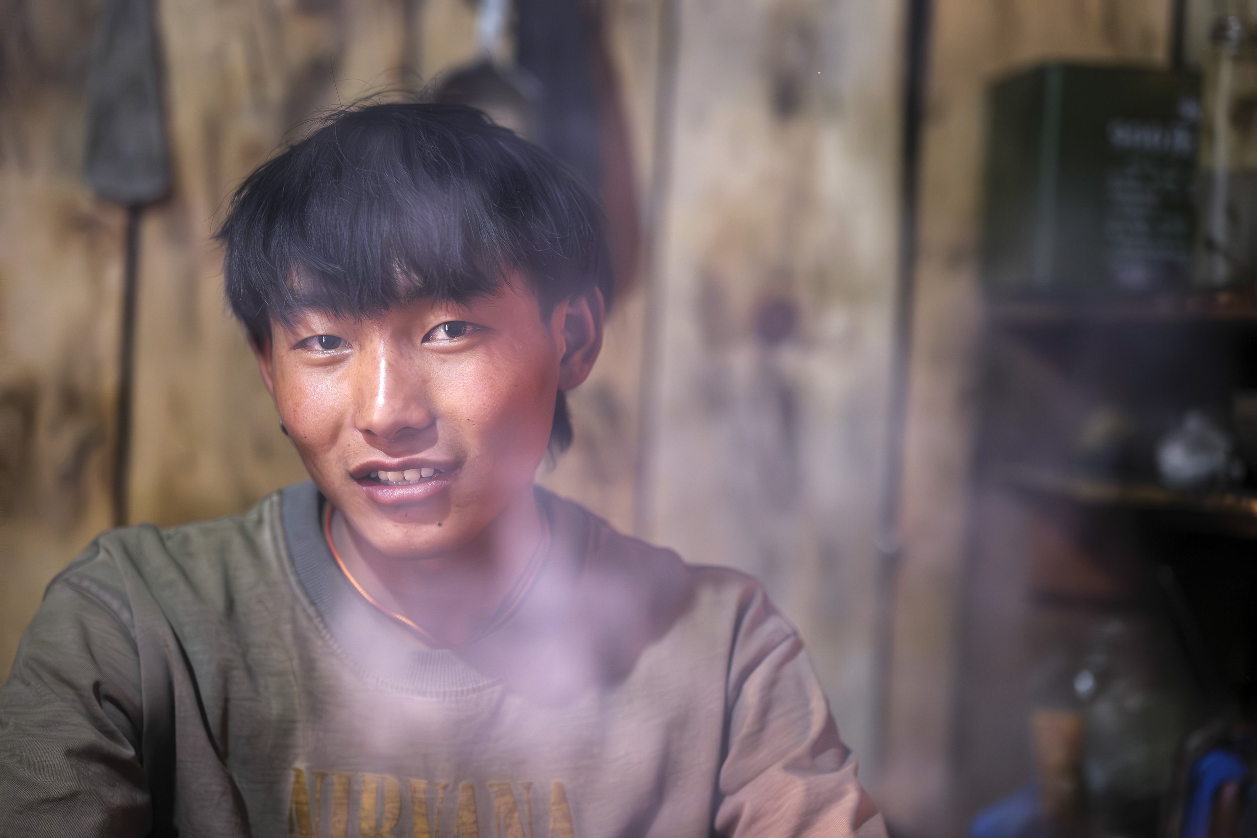 Sonam, a young guesthouse owner in Chumchet, pauses inside his kitchen as lunch simmers nearby. Tourism now shapes village livelihoods, and at his age, he balances cooking, hosting, and managing the guest house. Tsum Valley, Nepal. Photo By Steve Fag