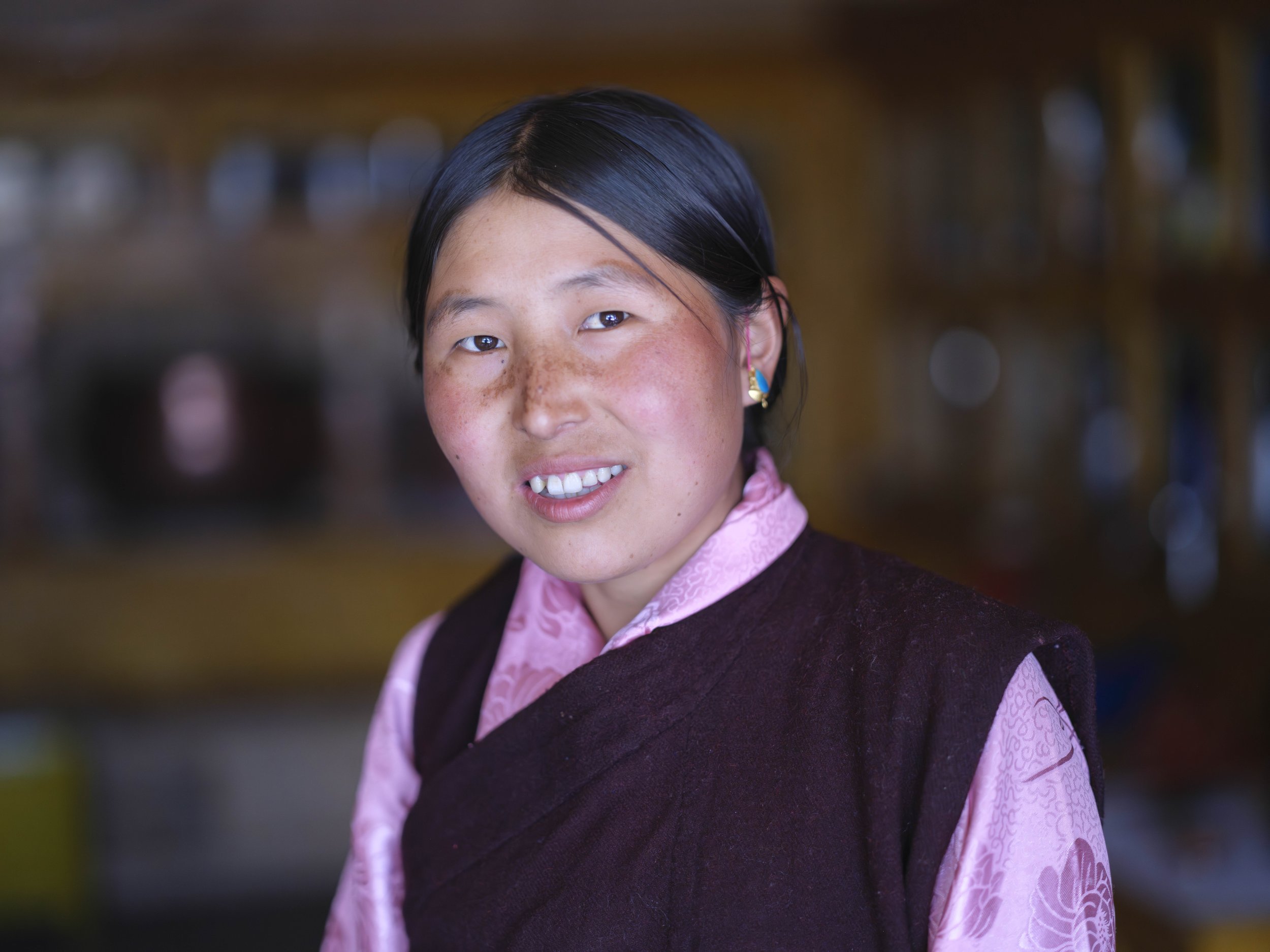 A Tsumba woman stands in her traditional dress, the layered chuba and handwoven fabrics reflecting generations of skill in Tsum Valley. Clothing here marks identity, marital status, and community ties, carrying history in its patterns and the pride o