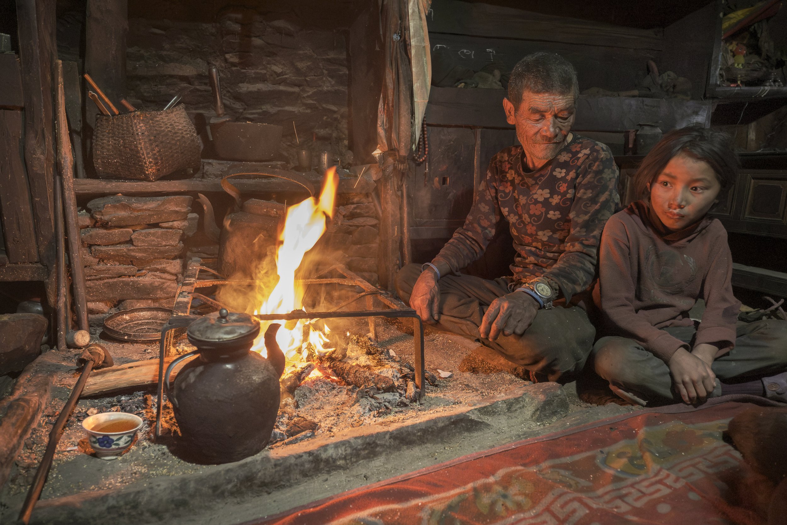 Dhawa Doma sits beside her grandfather in their traditional Tsum Valley kitchen, the hearth at the center of the room. At a tender age, she tends to the family’s animals and cares for her aging grandparents after her parents left the village to begin