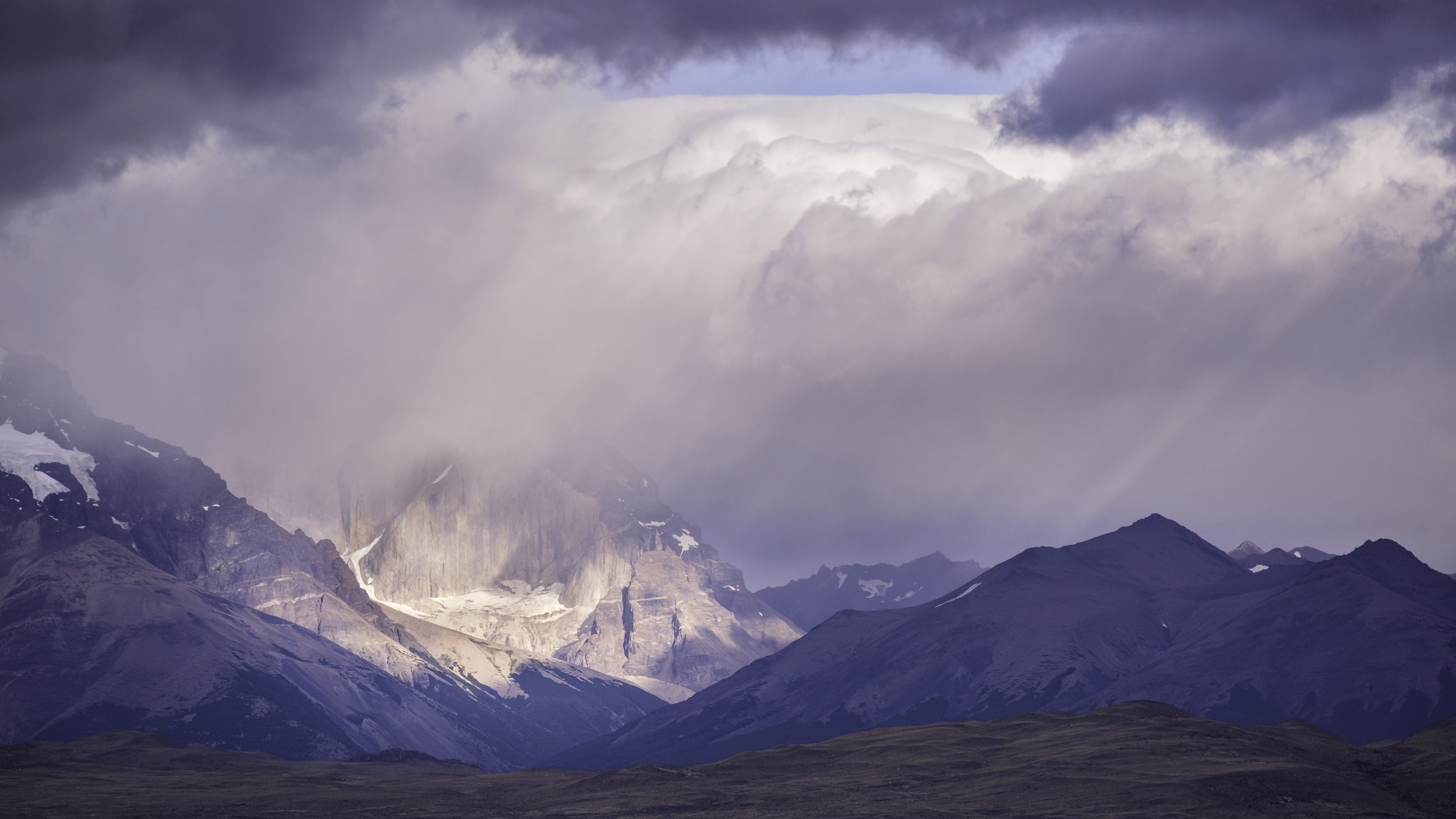 Mountain range with snow-capped peaks under cloudy sky