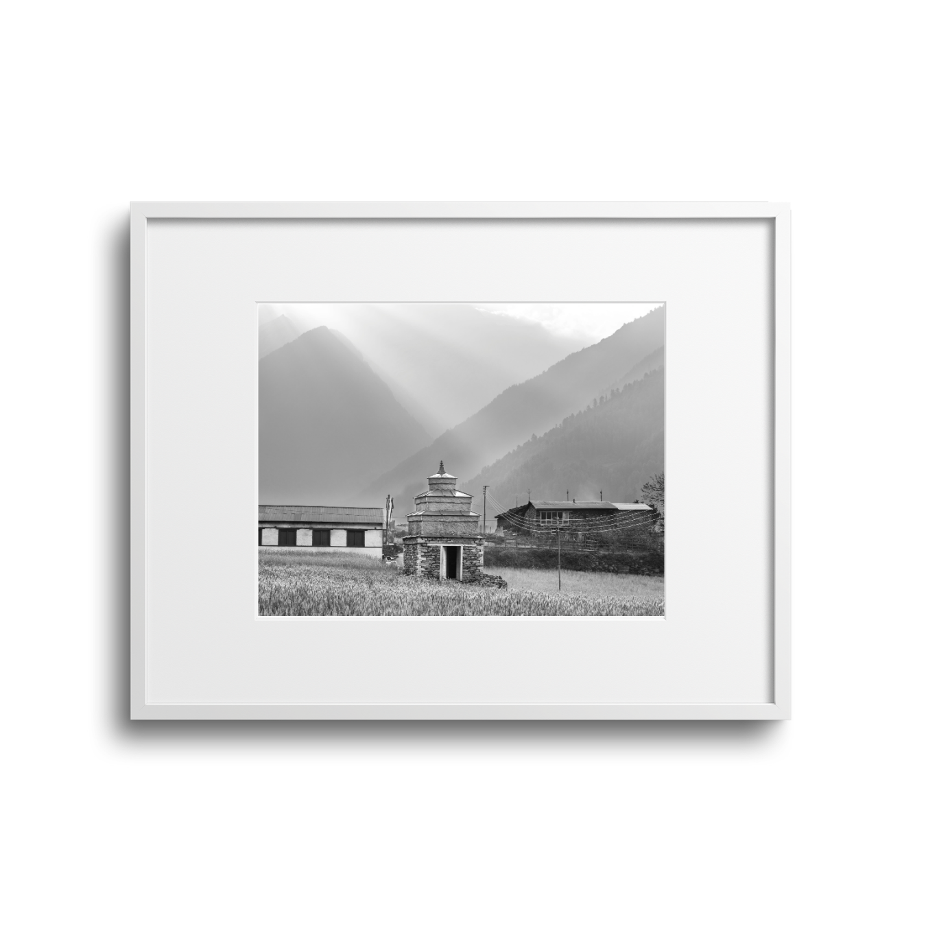 Black and white photo of a rural scene with mountains in the background, a small temple in the foreground, and traditional buildings nearby in a valley.