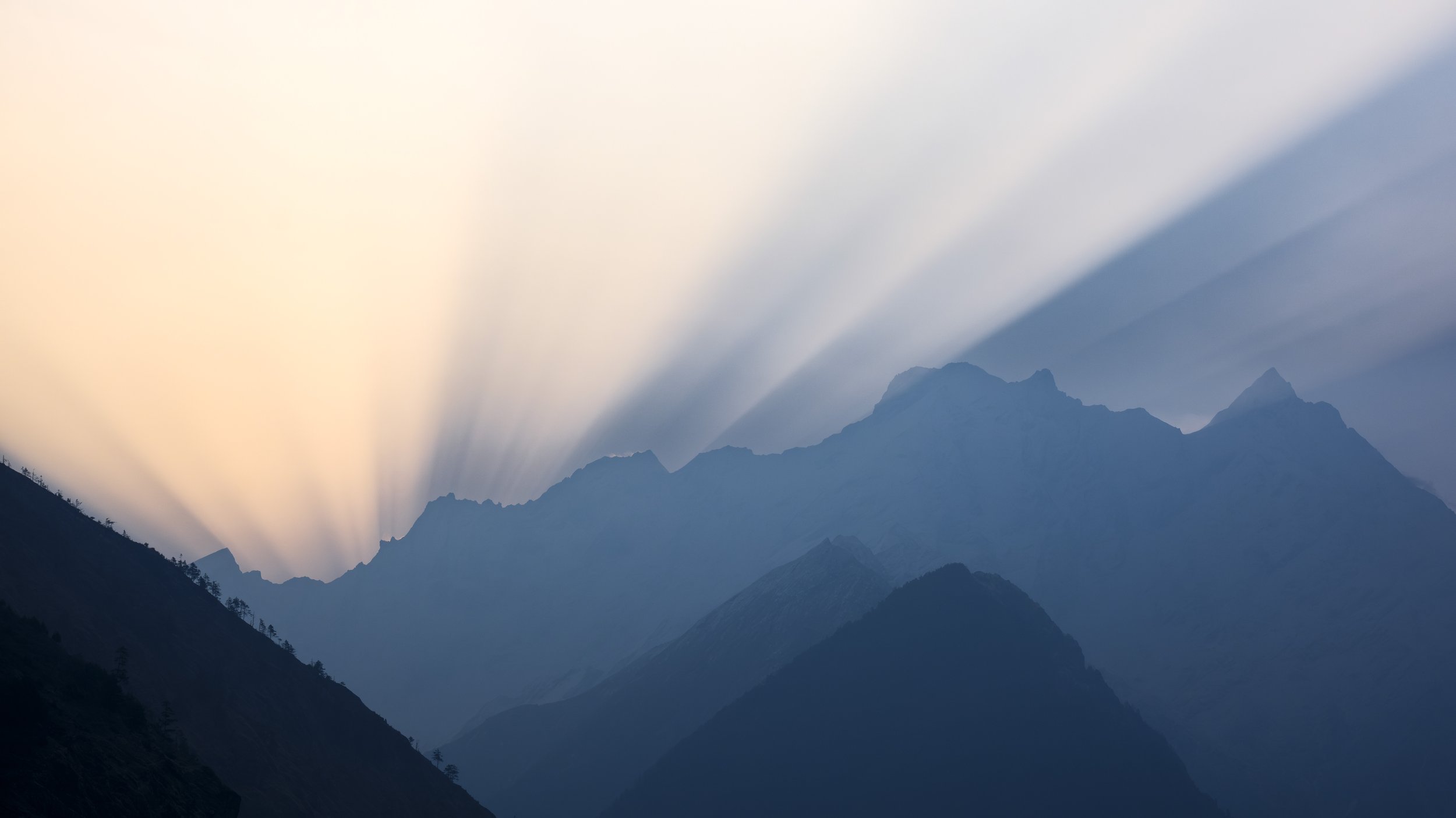 Mountain range silhouettes at sunset with sun rays shining through clouds.