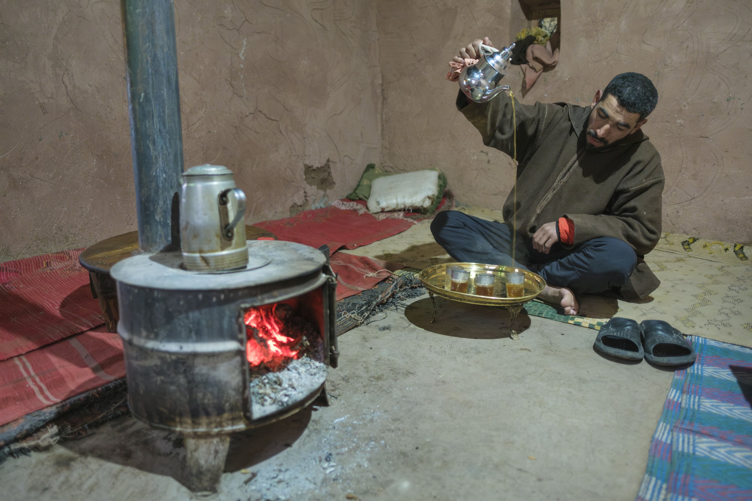 Man pouring Moroccan mint tea beside a wood stove inside a mountain home in Aït Bouguemez Valley, High Atlas Mountains. Photo by Steve Fagan
