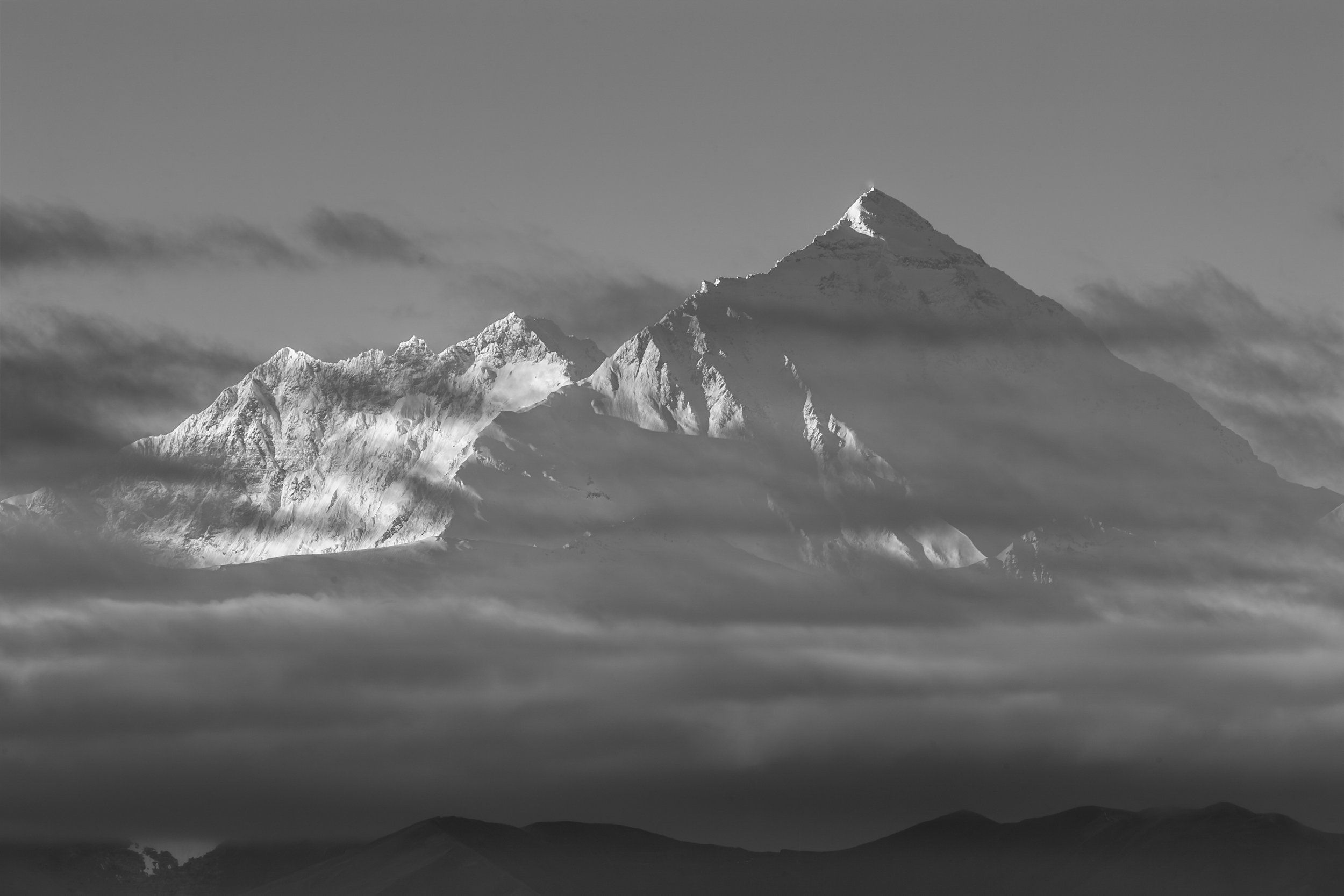 Mount Everest partially obscured by clouds rising above the Tibetan Plateau.