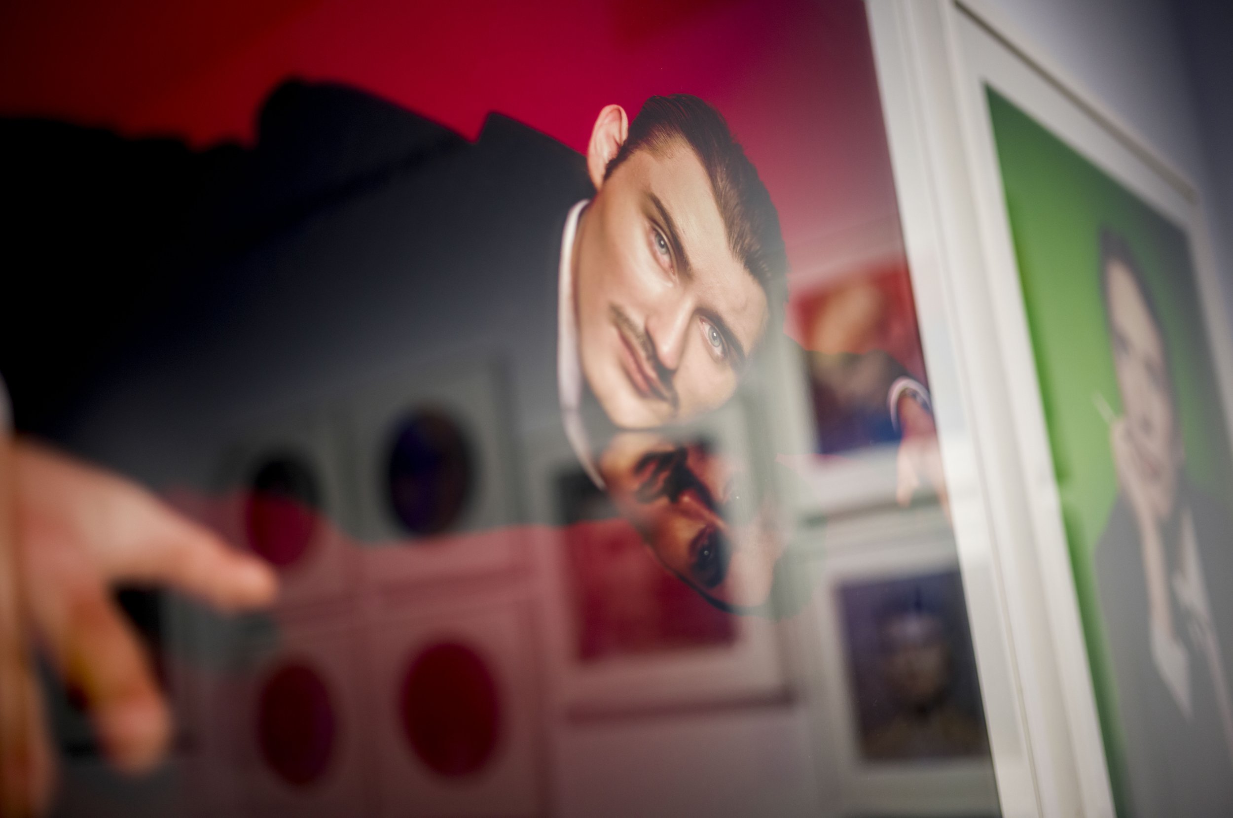 Portrait of a man distorted through reflective glass in a gallery space.