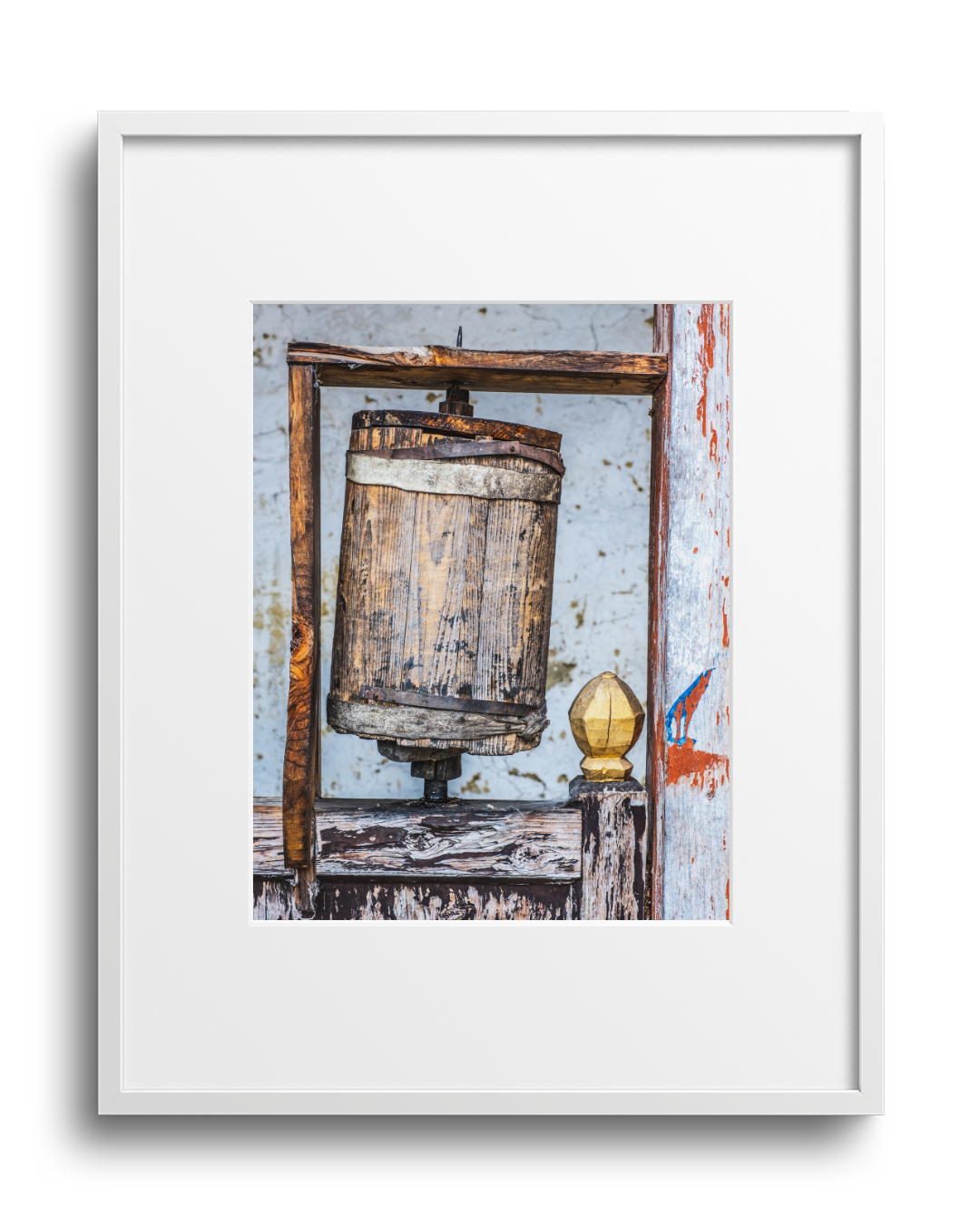 Close-up of an old wooden butter churn with a wooden dasher, sitting on a weathered wooden surface near a chipped white wall.
