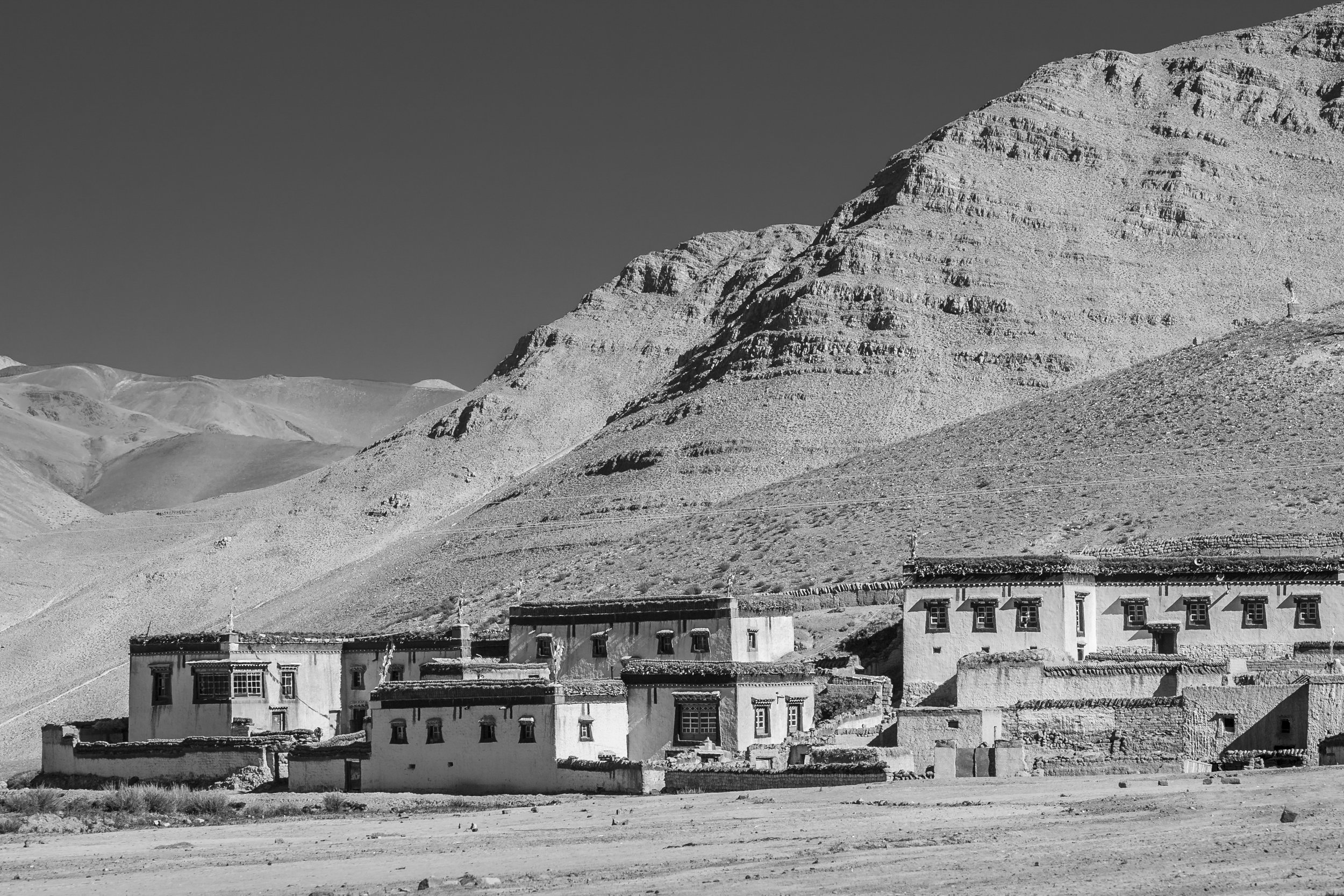 Traditional Tibetan buildings at the base of a barren mountain landscape on the plateau.