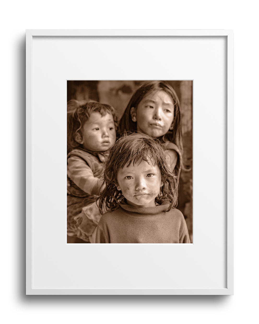 A sepia-toned photograph of three children, a girl and two younger children, looking directly at the camera, framed in a white border.