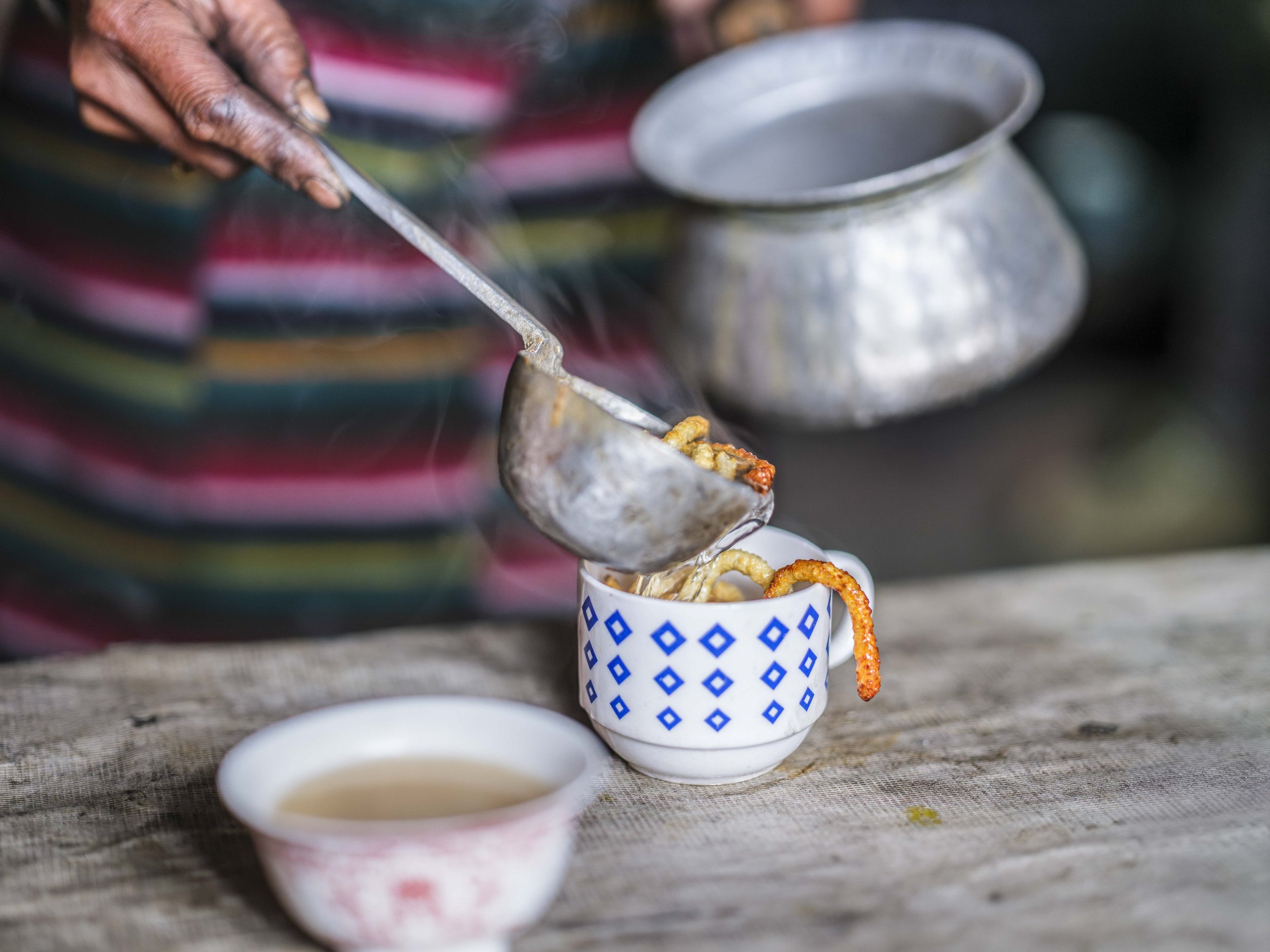 A steaming cup of rakshi, the locally brewed alcohol, is served with deep-fried yak cheese (churpi). The churpi slowly softens in the hot liquid, releasing a smoky, earthy flavor that enhances both taste and warmth, a mixture cherished in the high Hi