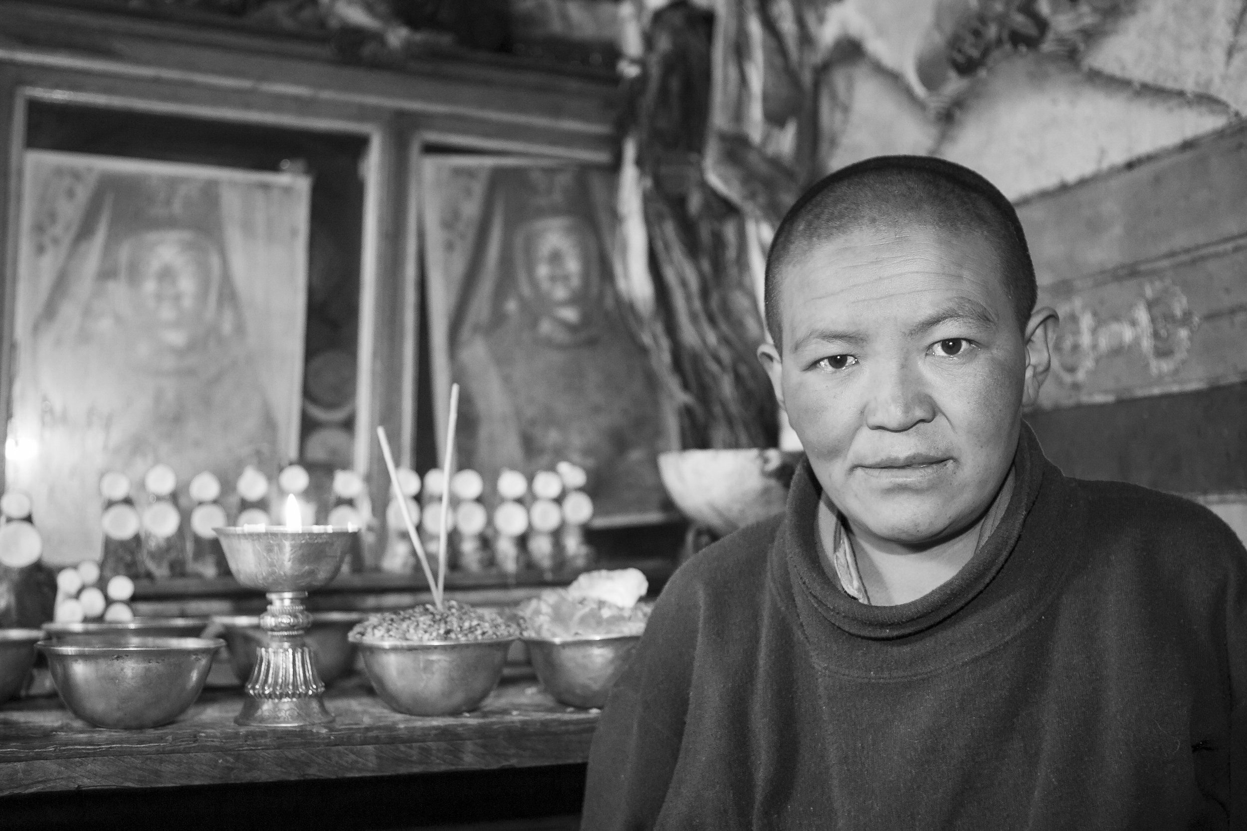 Buddhist nun seated inside a monastery with candles and ritual objects in Tibet.