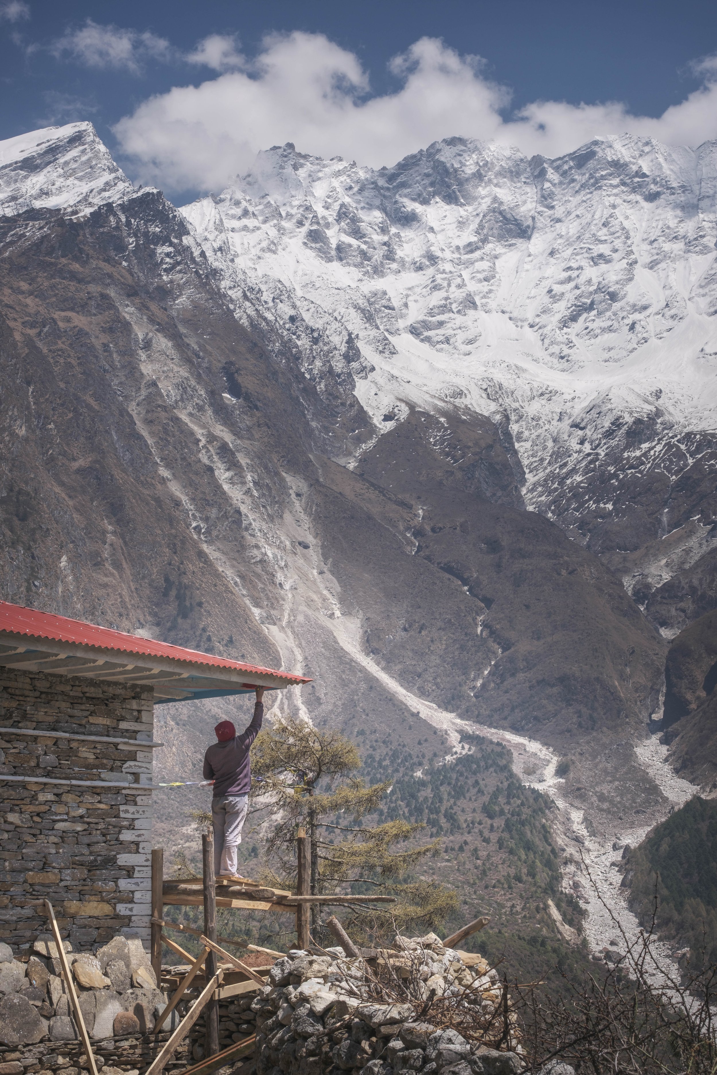 Man repairing the roof of a stone house overlooking a high mountain valley in Tsum Valley, Nepal.